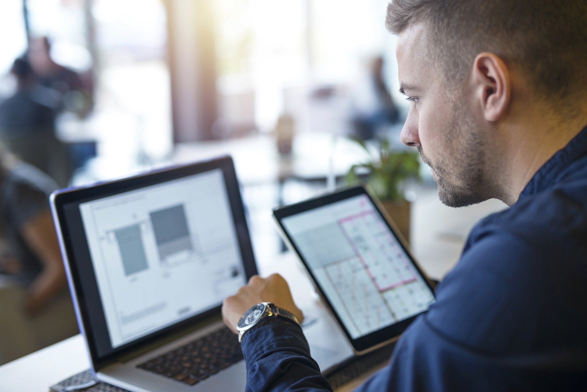 man working with a laptop and tablet against a blurred background