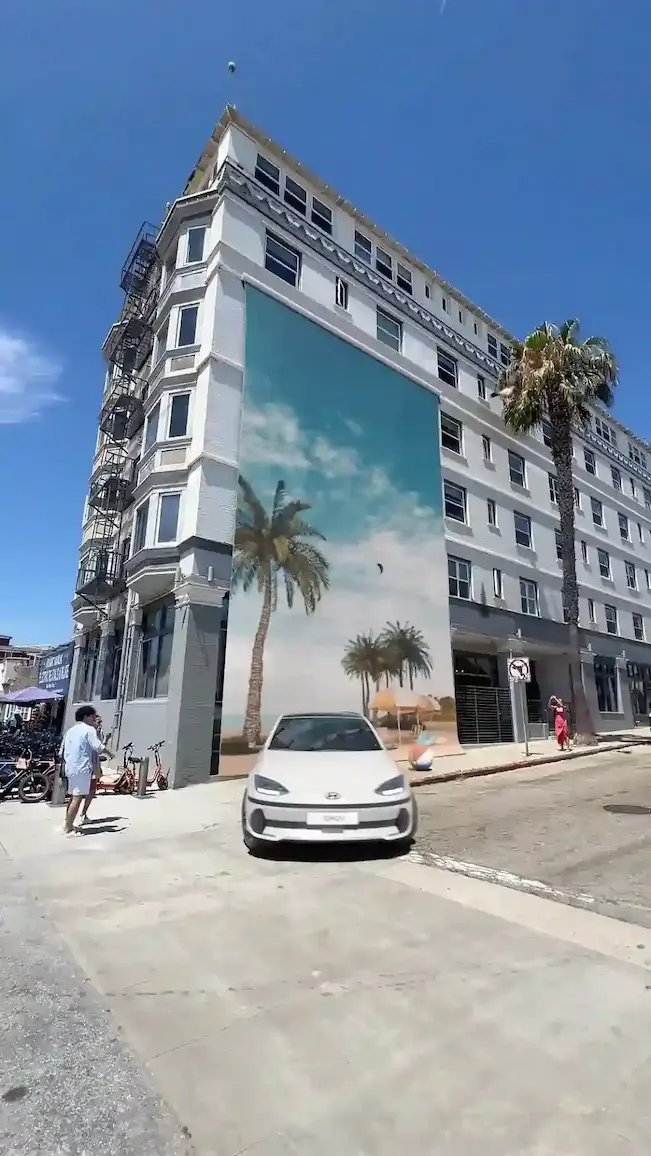 A white Hyundai car in front of a massive beach-themed mural on a city building