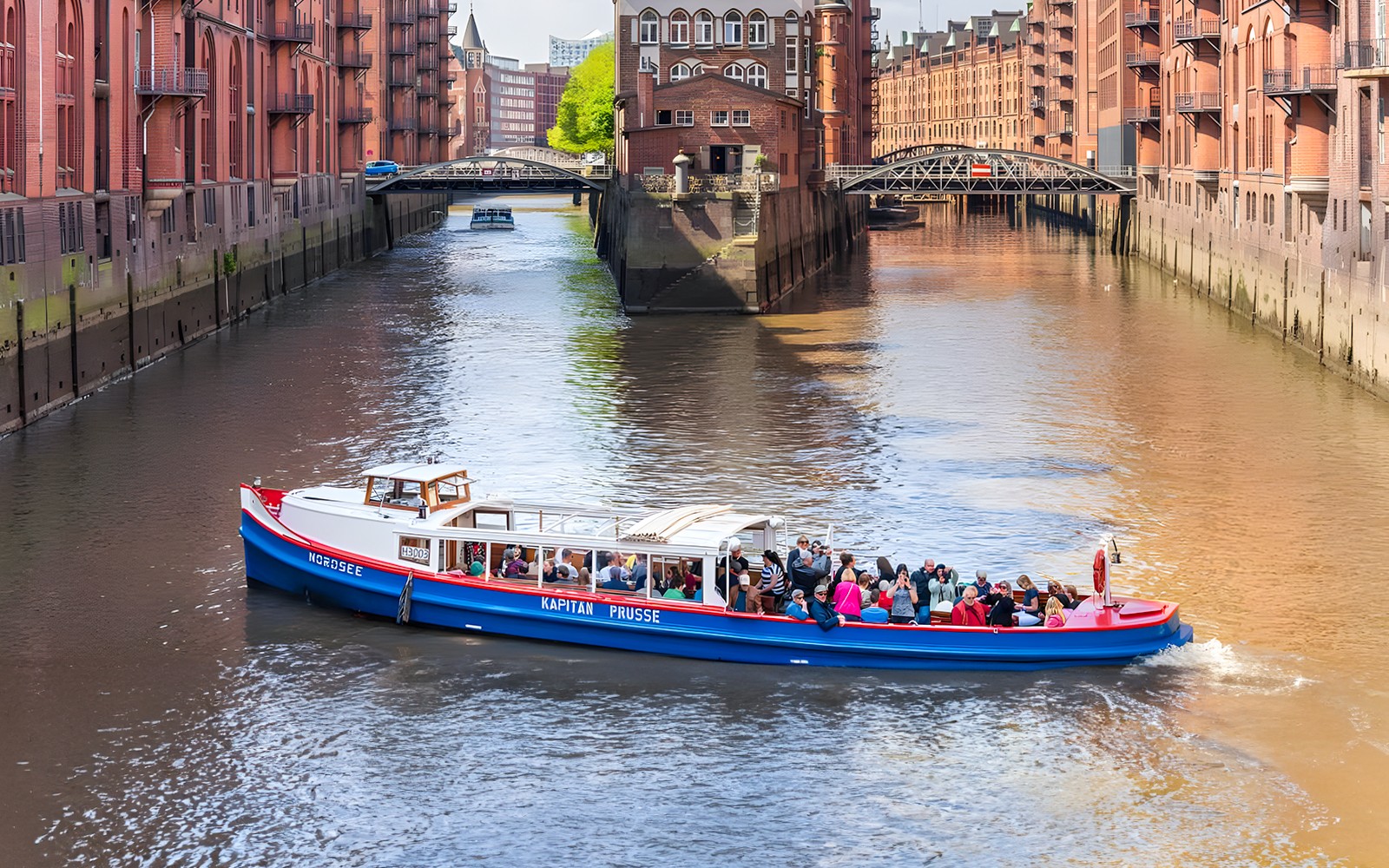 Harbor cruise boat with tourists on a canal in Hamburg's Speicherstadt district.