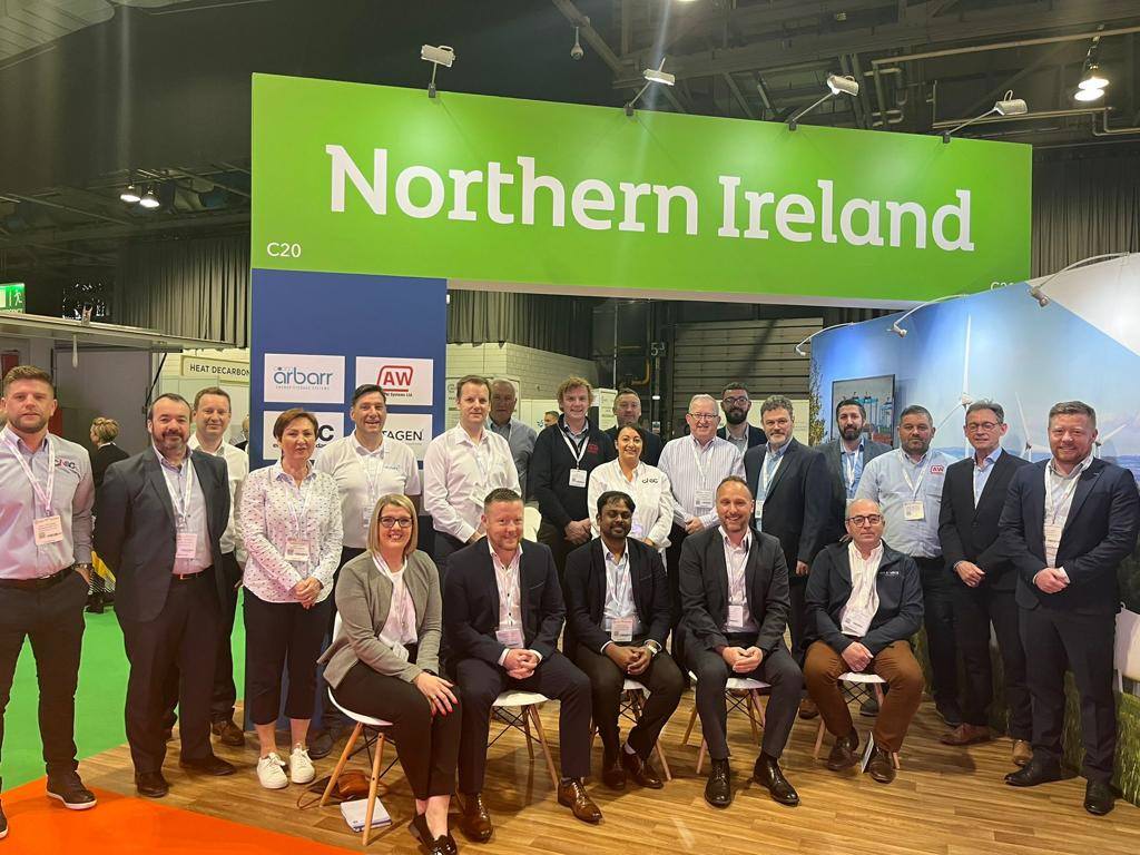 Large group of people posing together at an exhibition stand labelled ‘Northern Ireland’