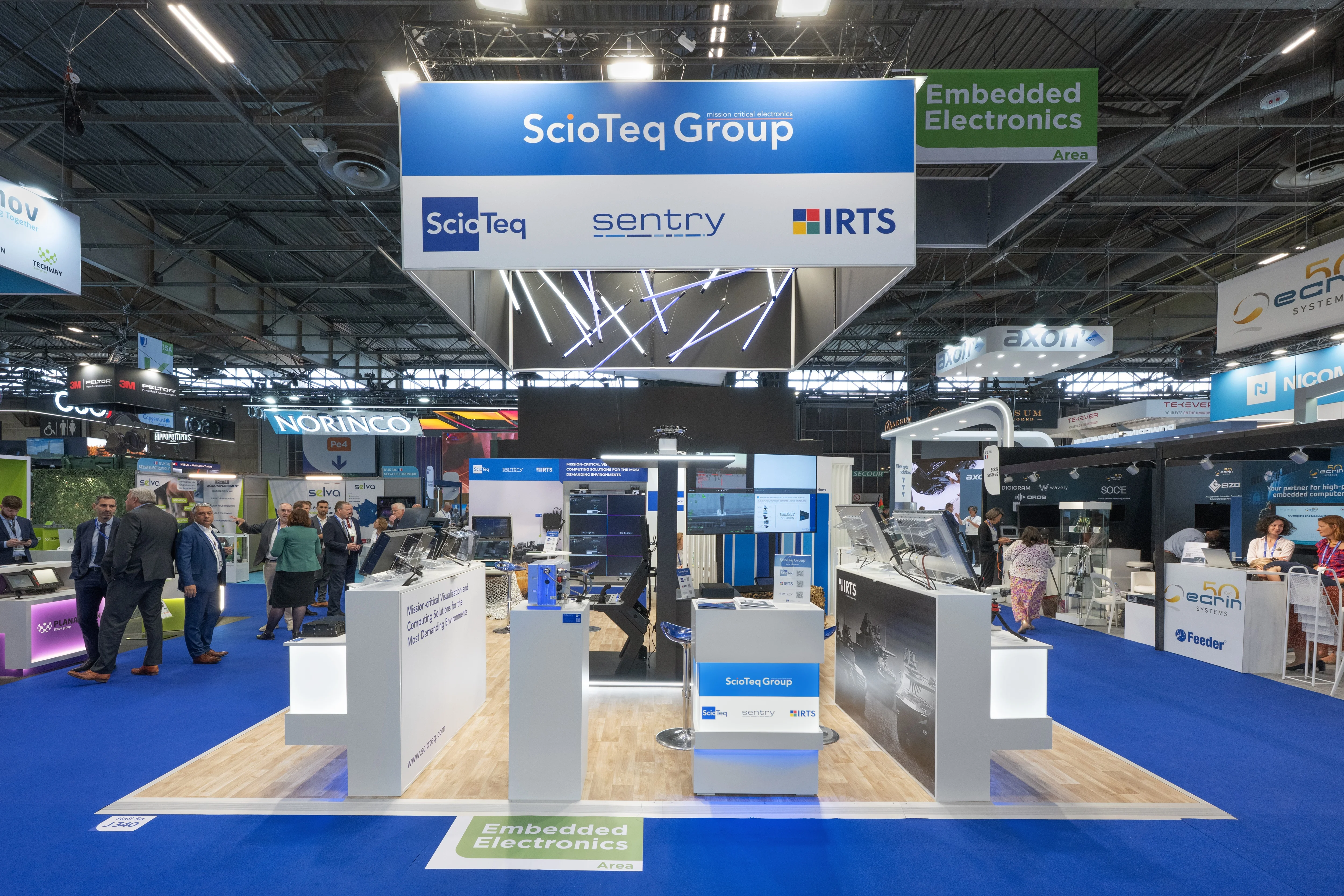 Stand IRTS / ScioTeq Group conçu et réalisé par Expace à Eurosatory 2026 – espace sur-mesure défense avec bandeau suspendu lumineux, comptoirs de démonstration d'écrans durcis et de calculateurs embarqués (ScioTeq, Sentry, IRTS).