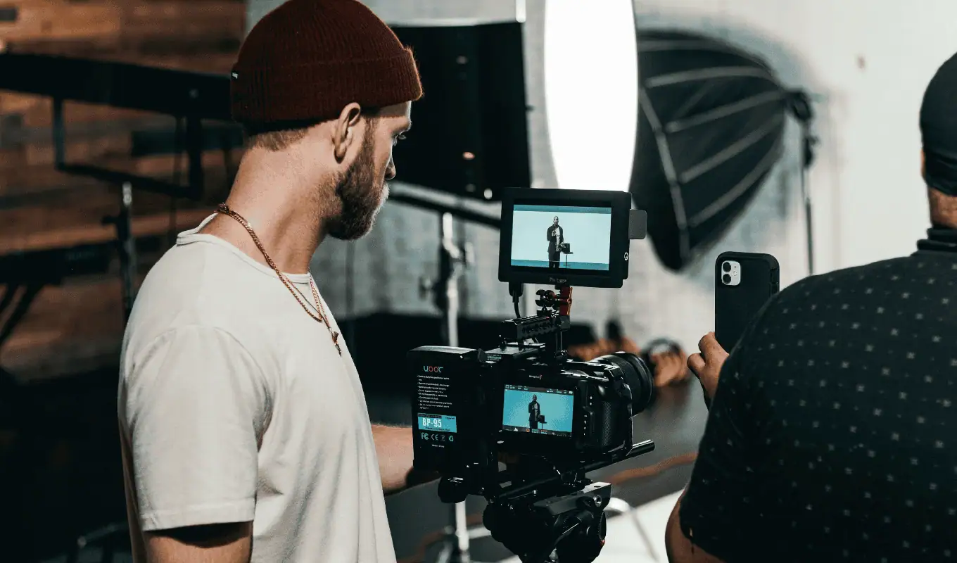 man in white polo shirt standing in front of black video camera