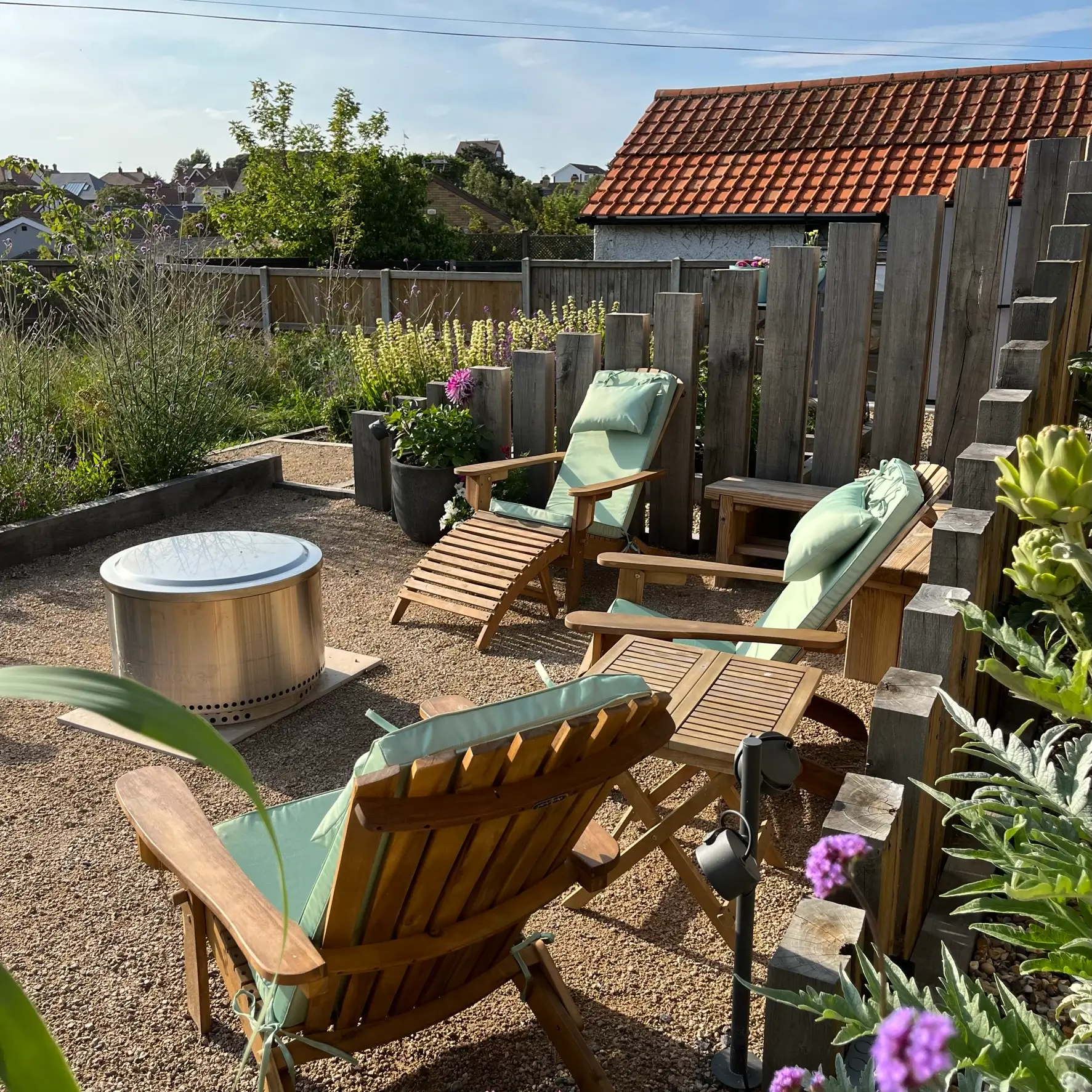 A cozy garden patio with two chairs, a small table, and lush greenery under a clear blue sky.