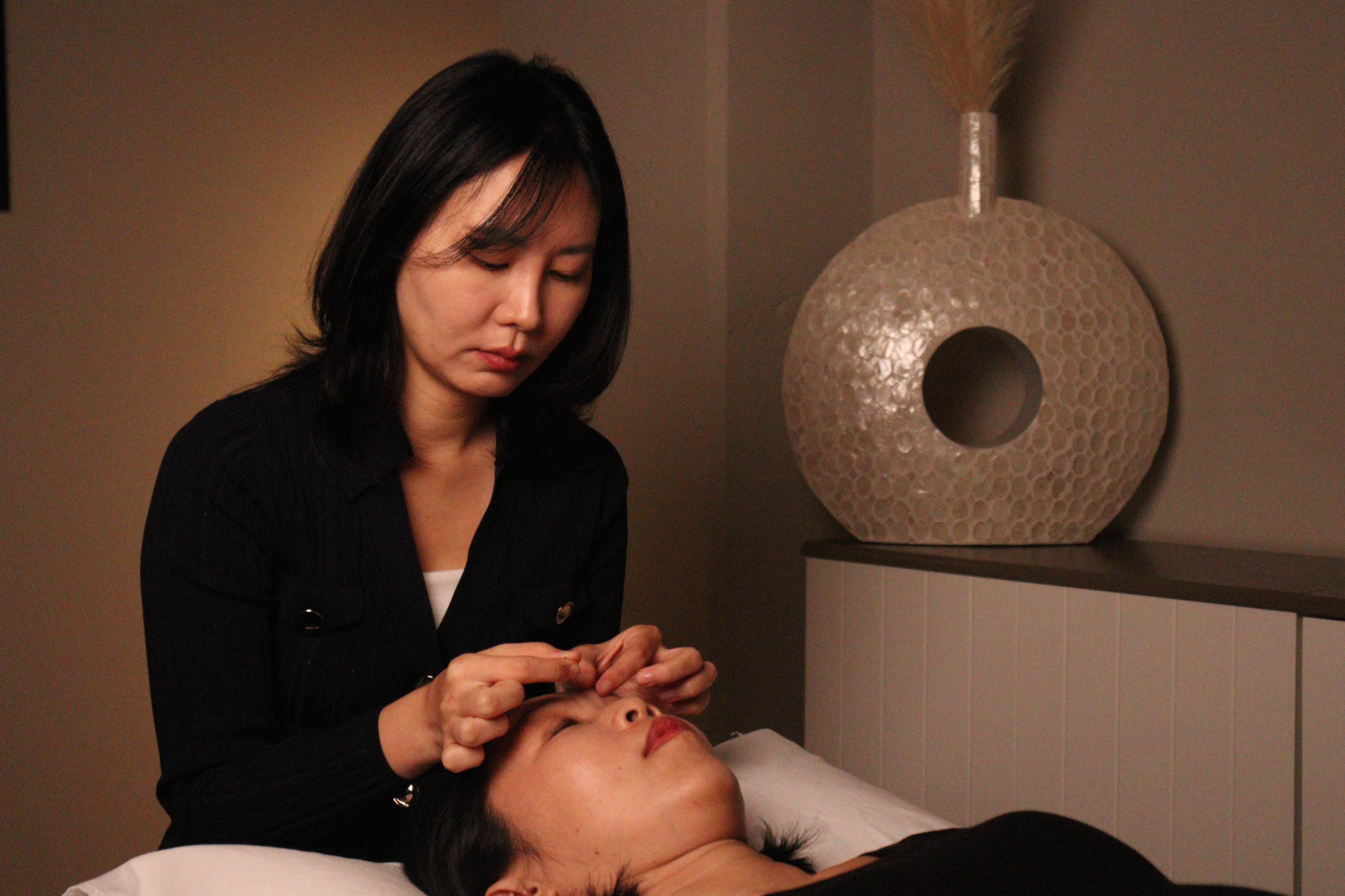 Female practitioner doing  facial acupuncture on a patient in a dimly lit treatment room
