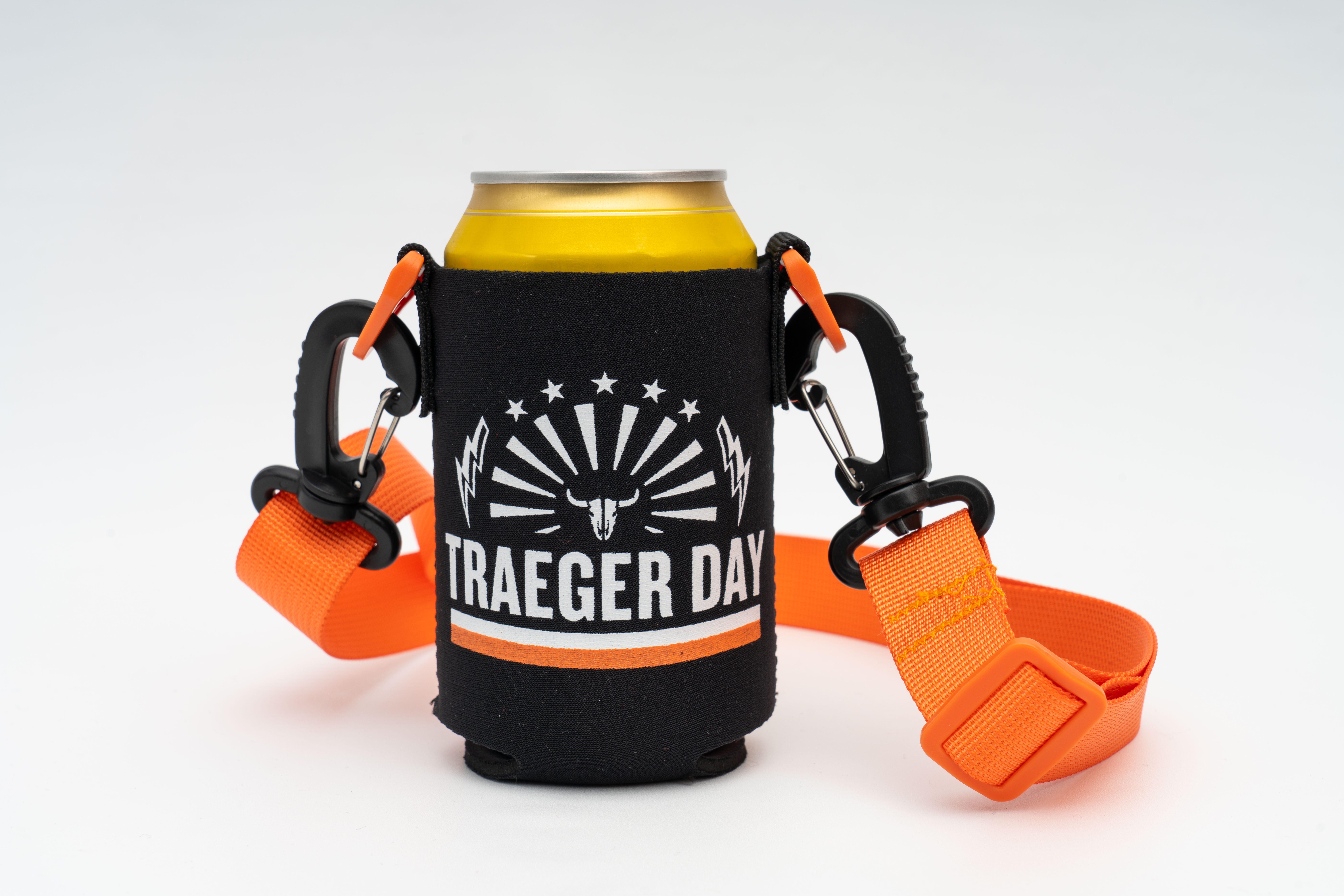 An image of a black drink insulator with an orange strap. On the front center of the insulator is the Traeger Day logo. The drink insulator is photographed against a white surface.