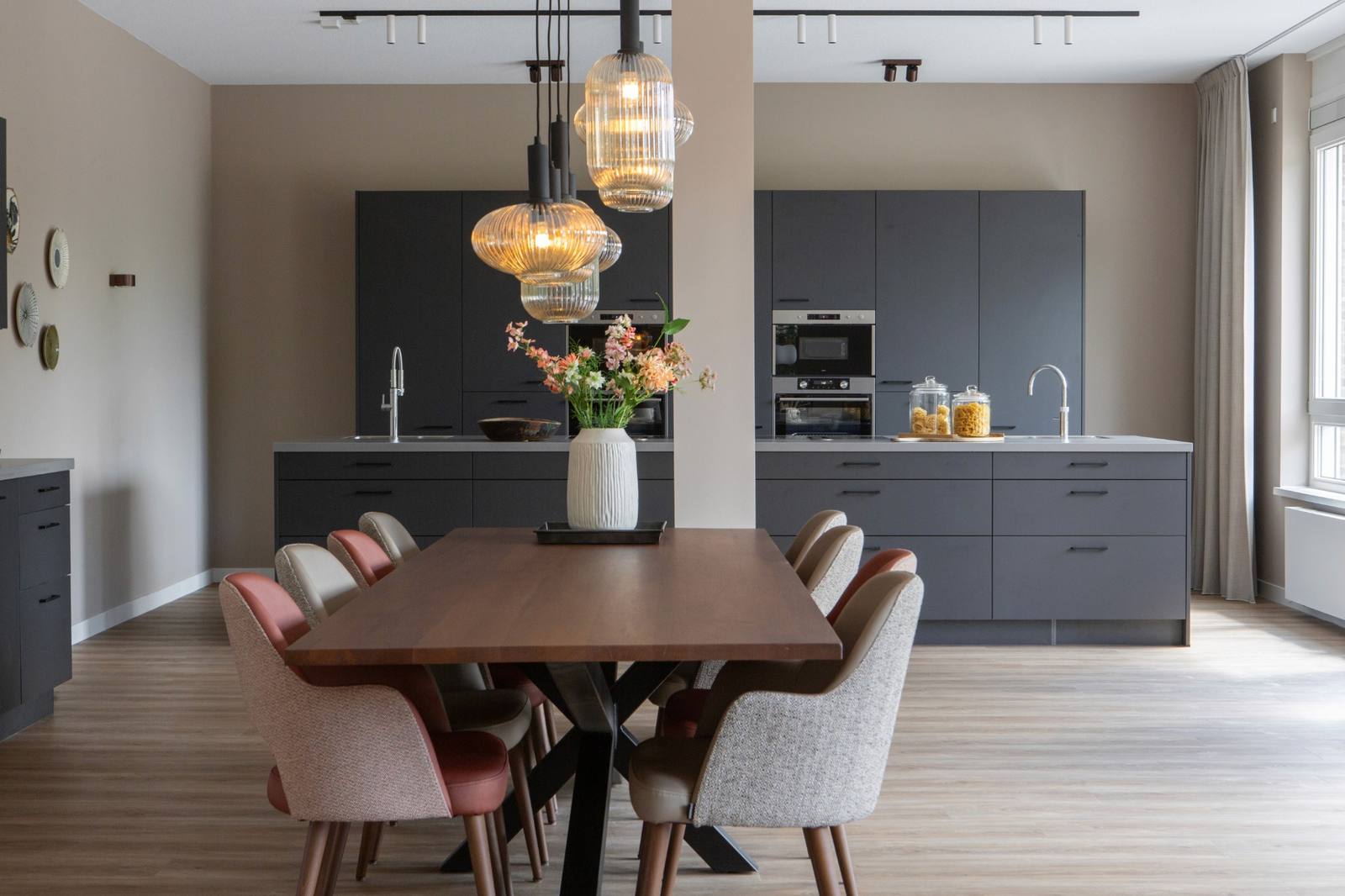 woonkeuken grijs met eettafel en gekleurde stoelen en groep glaslampen