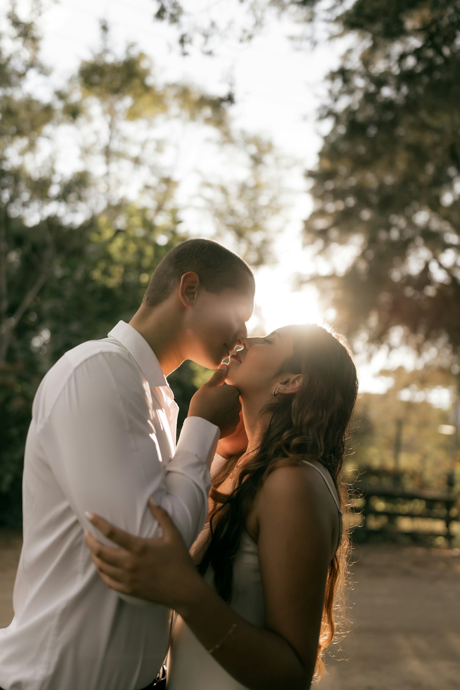 Couple kissing in soft sunlight beneath trees