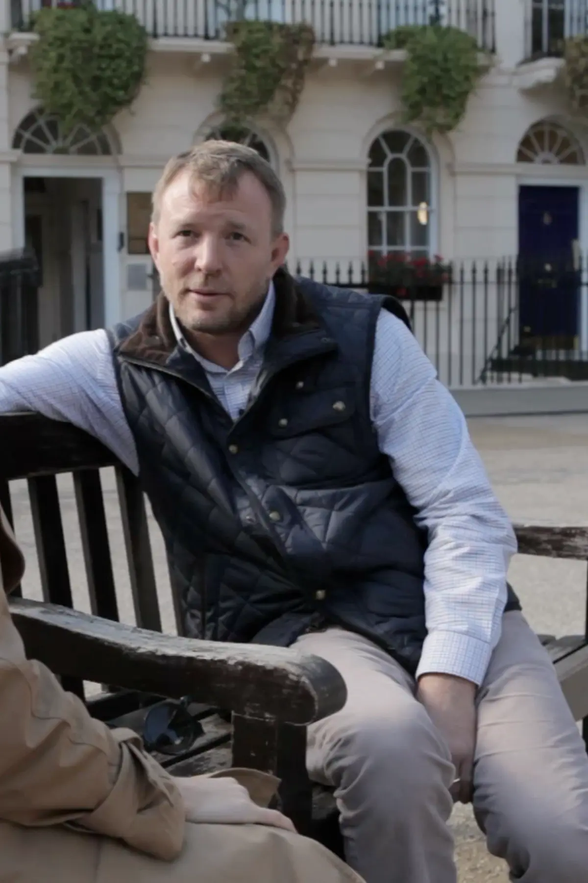 Guy Ritchie seated on a bench in London during a filmed conversation for the documentary