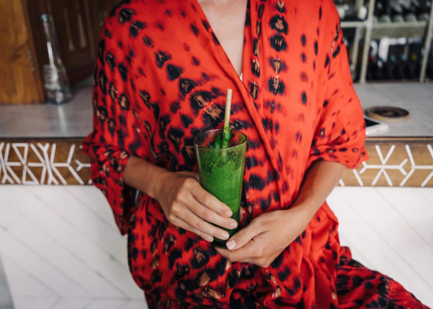 Woman in red and black robe holding glass with green juice to showcase the sirtfood diet for weight loss