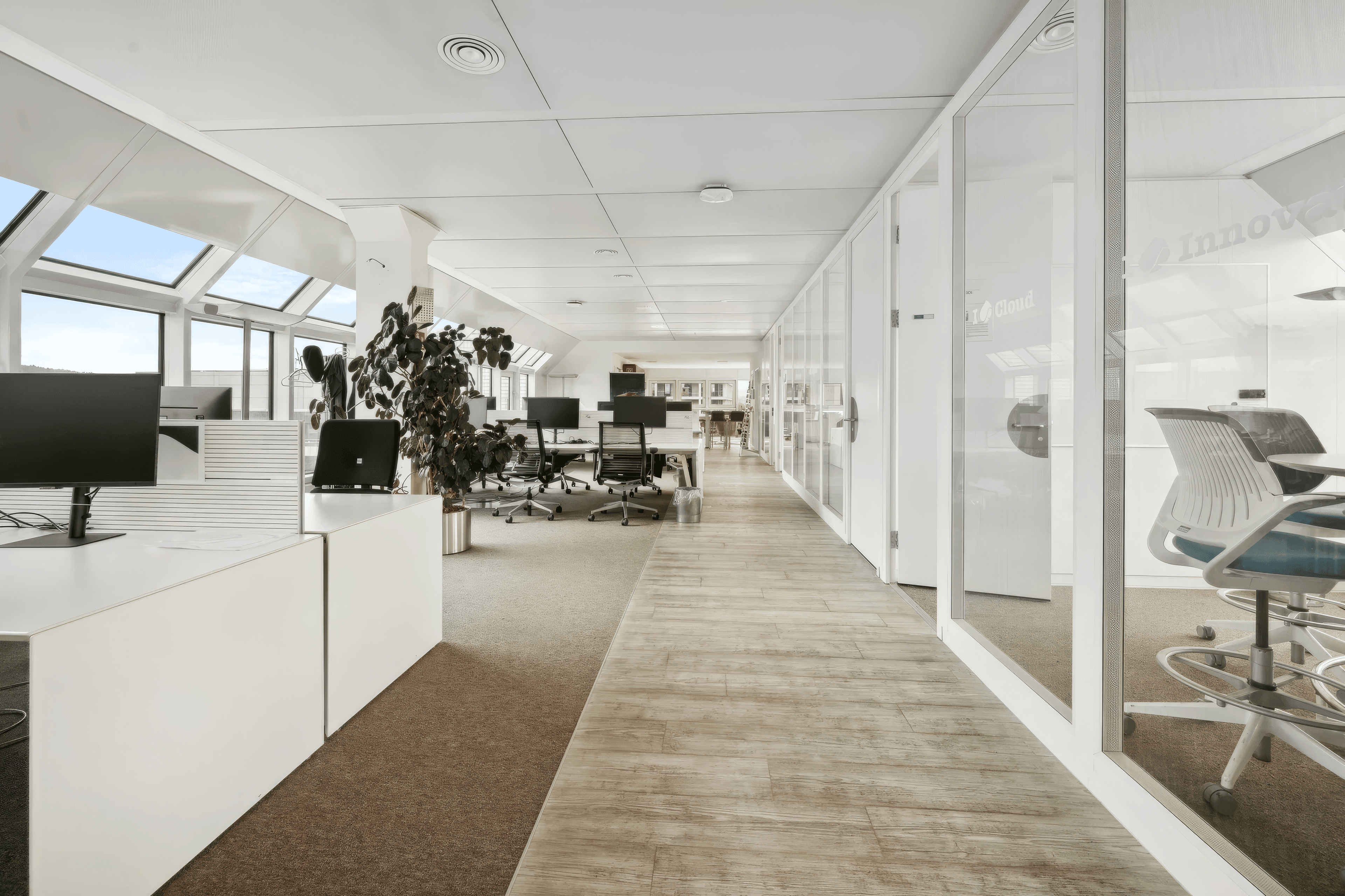 Modern office space with large windows, glass walls, and sleek furniture, bathed in natural light.