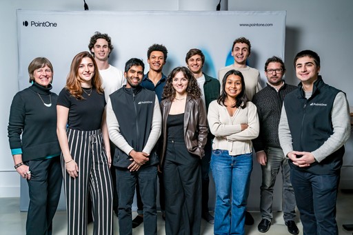 A diverse team of eleven smiling PointOne employees stands united against a branded backdrop, reflecting a collaborative.