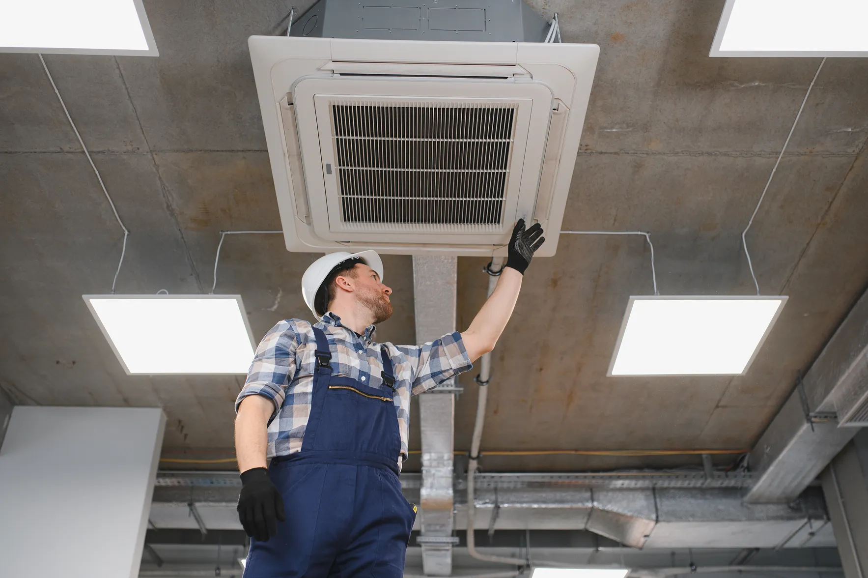 Close-up of hands in protective gloves removing a dirty air filter from an AC unit for cleaning or replacement.