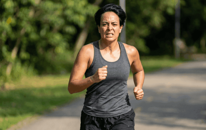 Mulher correndo na rua e com expressão de esforço acima do normal.