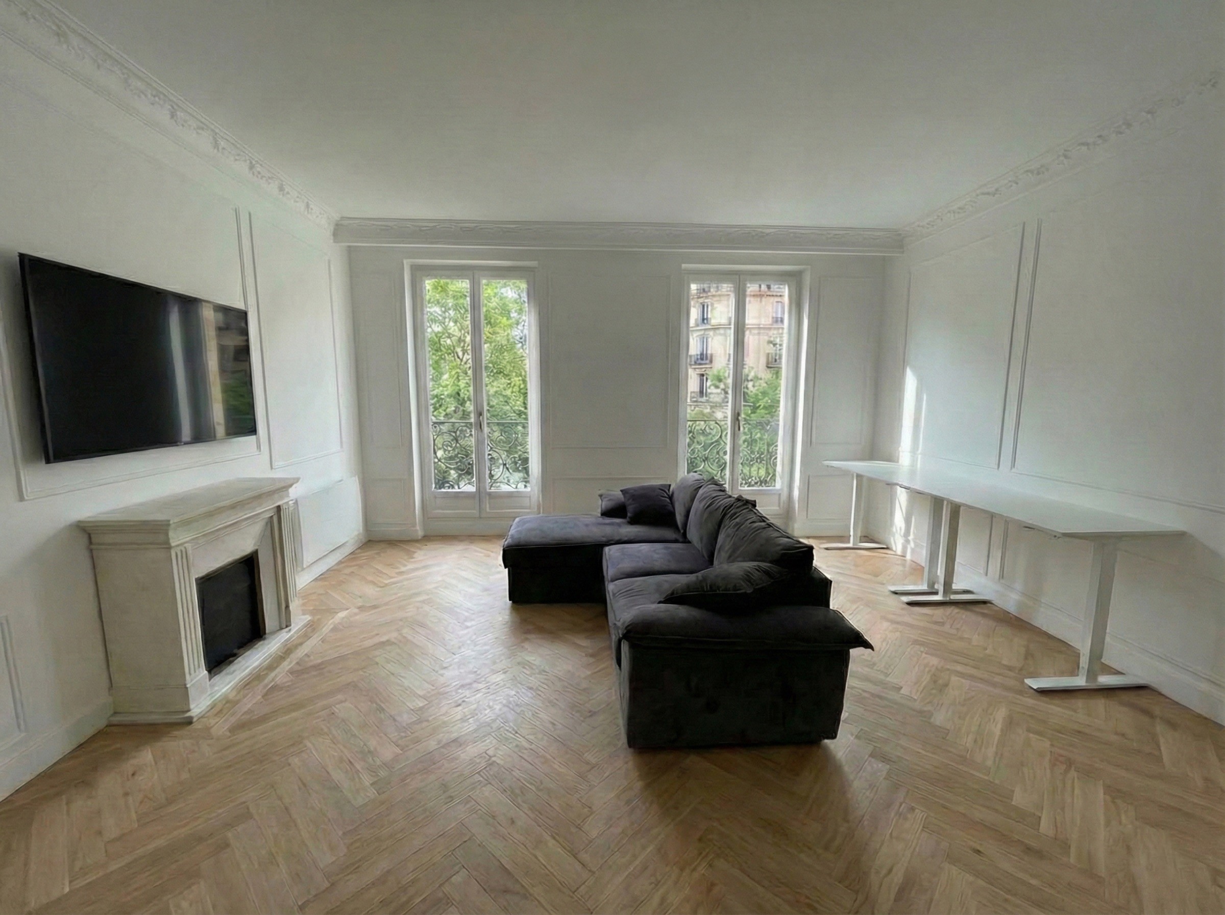 Salon haussmannien rénové avec parquet point de Hongrie, cheminée ancienne en marbre blanc et canapé d'angle anthracite.