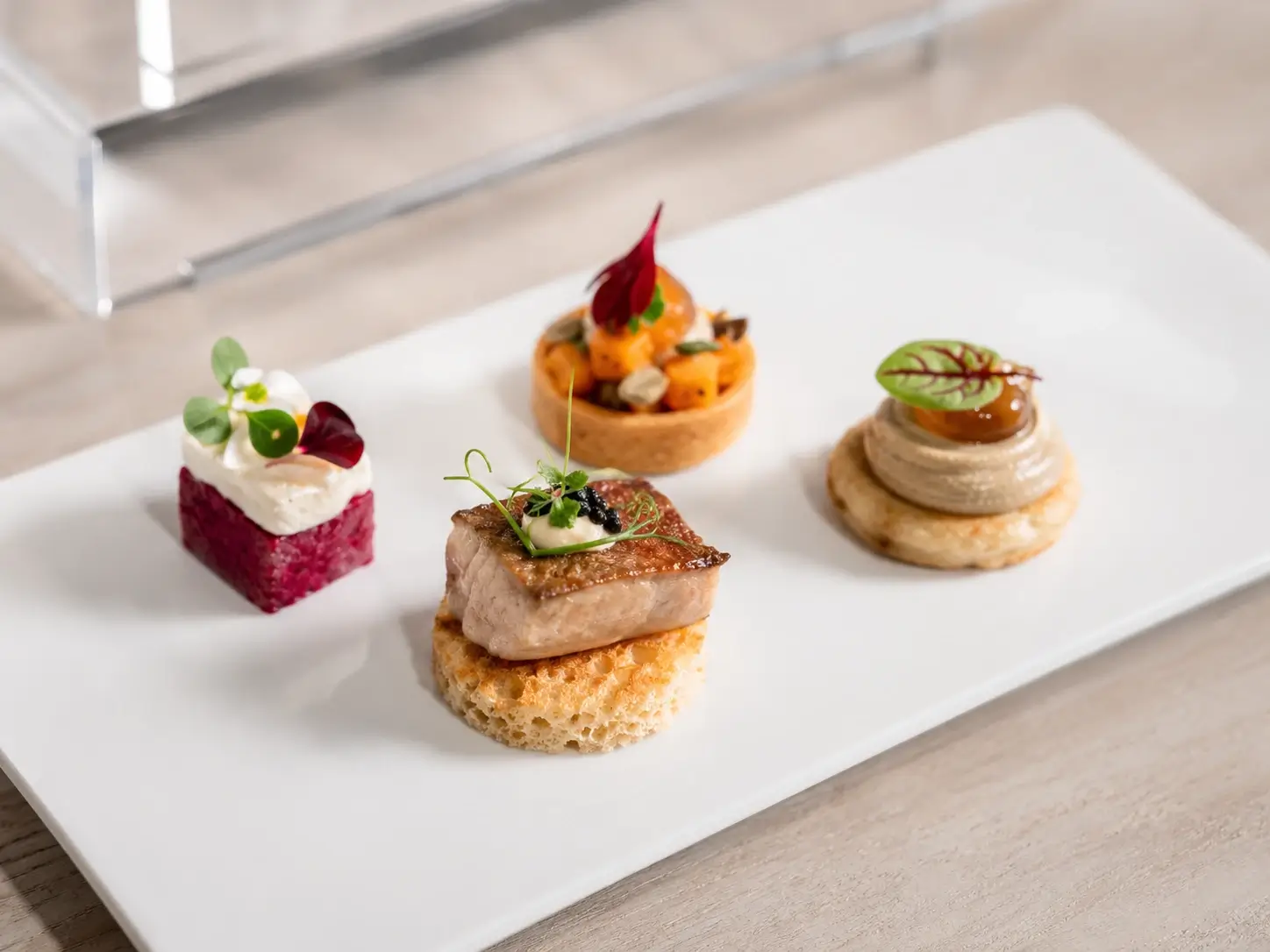 Buffet para coquetel de empresa em São Paulo com quatro canapés autorais finger food sobre louça branca executiva