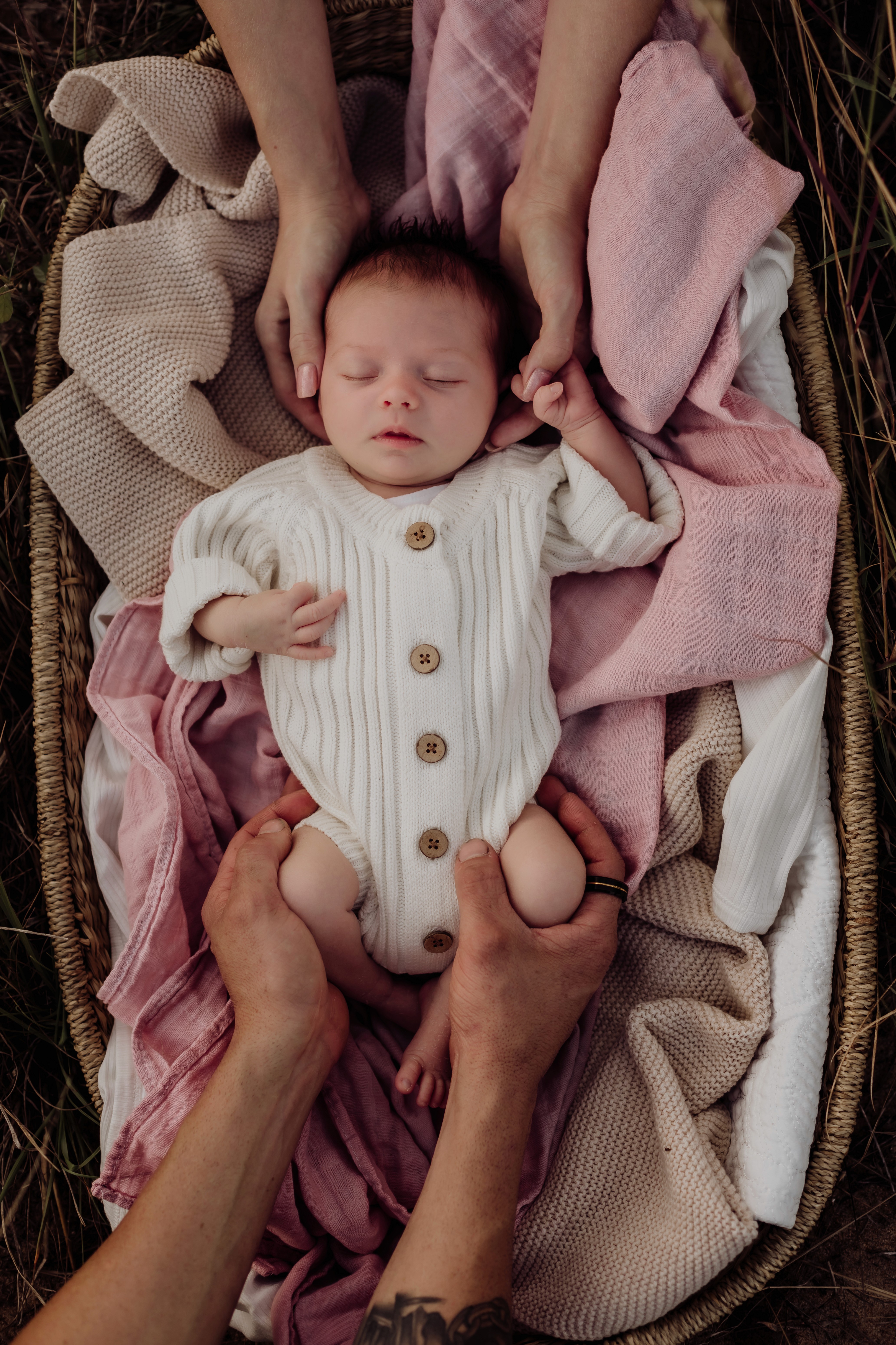 Newborn baby sleeping in basket with parents hands comforting, in an outdoor newborn photography session in Mackay