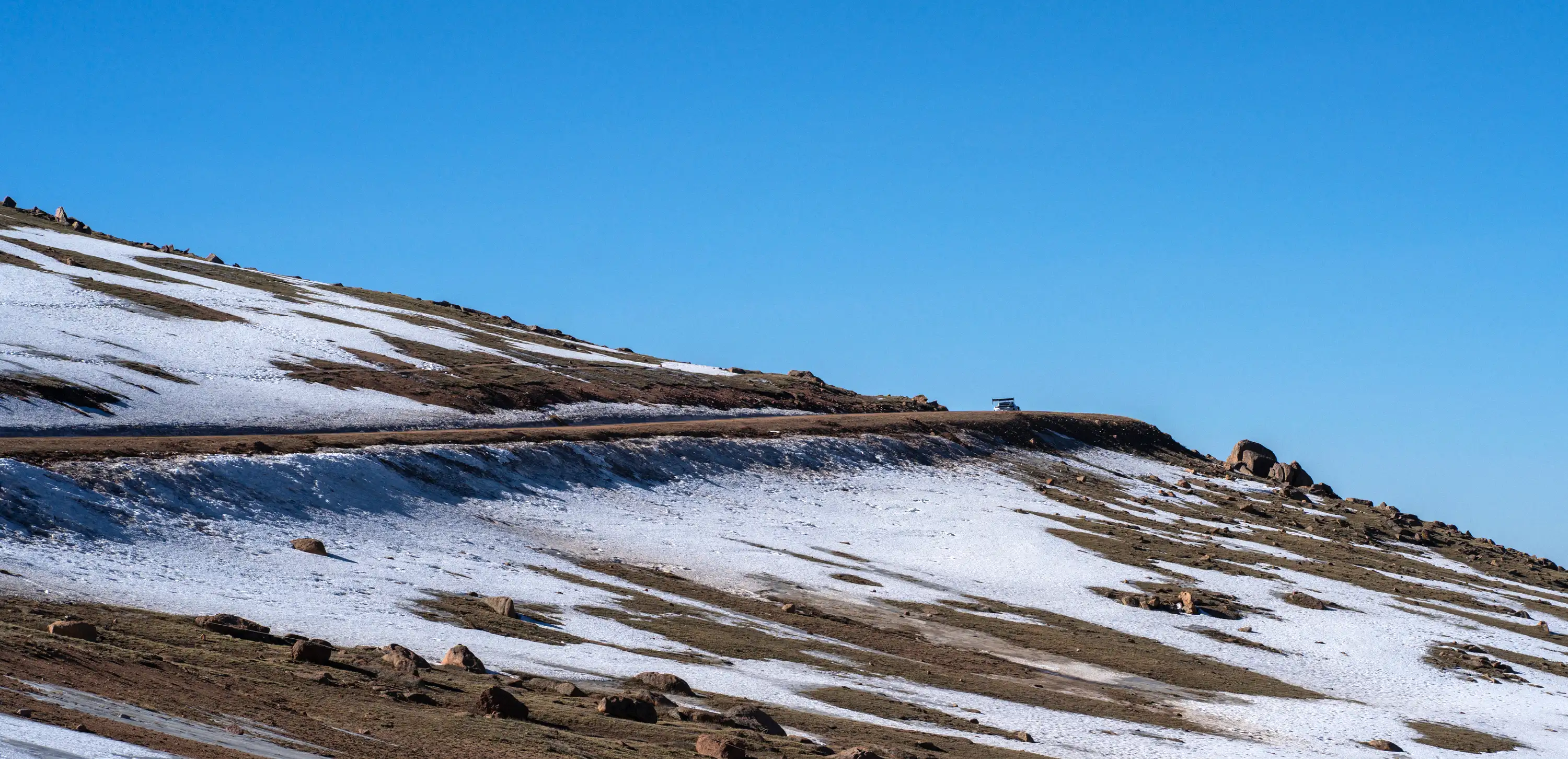 A race car driving up Pike Peaks mountain, with snow on the ground.