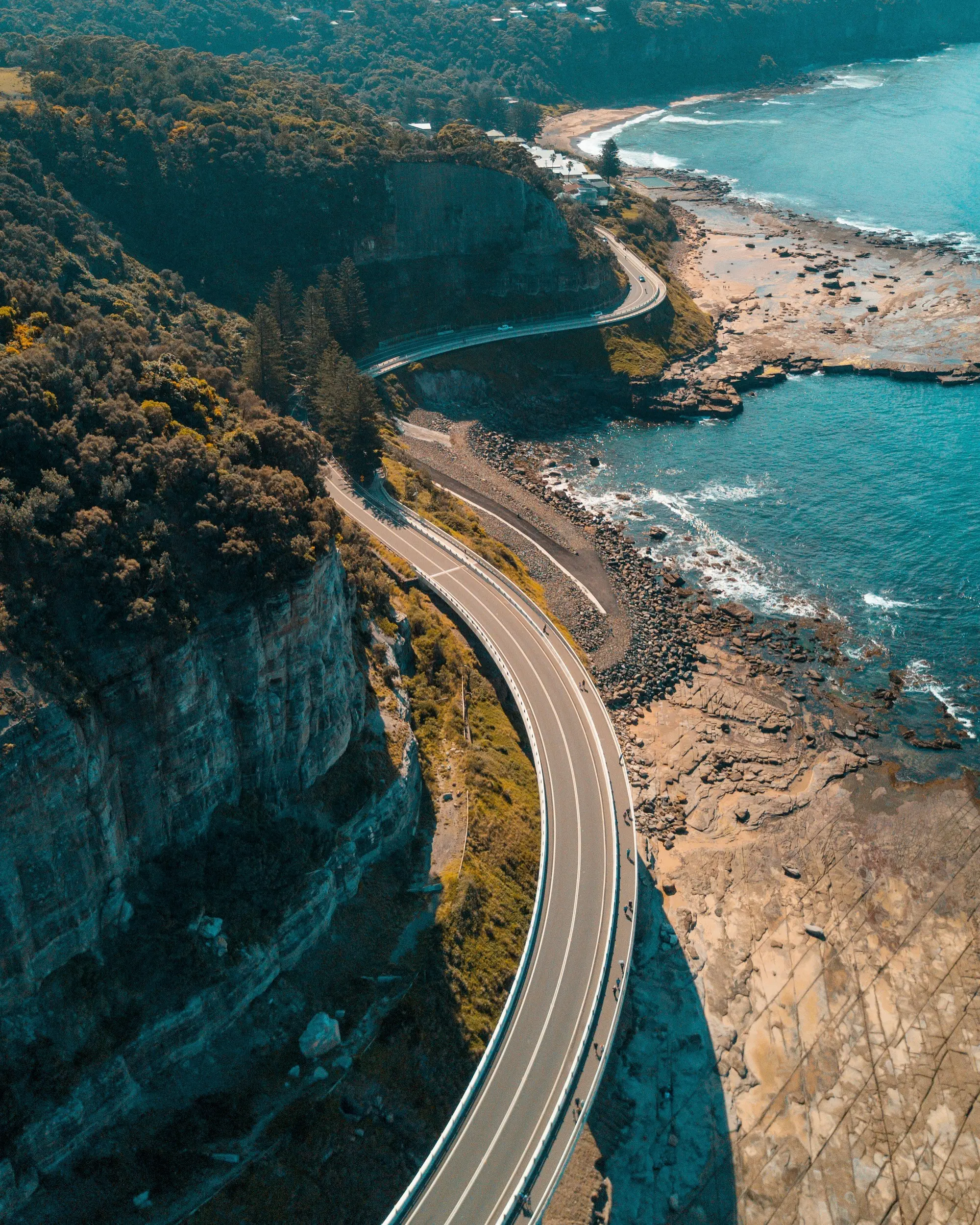 Aerial view of a coastal highway curving along the ocean, representing roadside assistance services