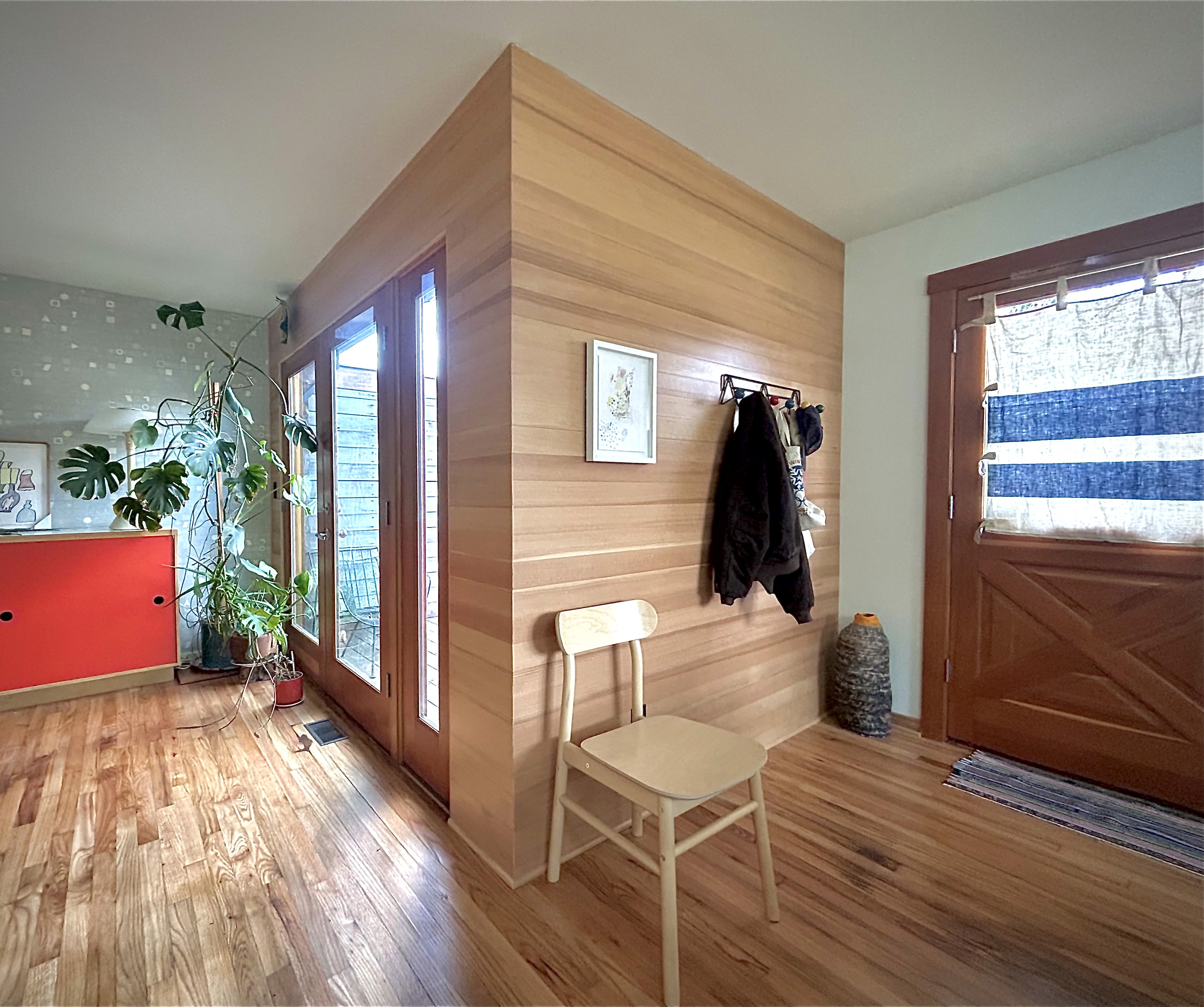 Horizontal bands of Douglas fir wood create an interior wall surface from the front door of a condo and wraps around another wall with a balcony door.