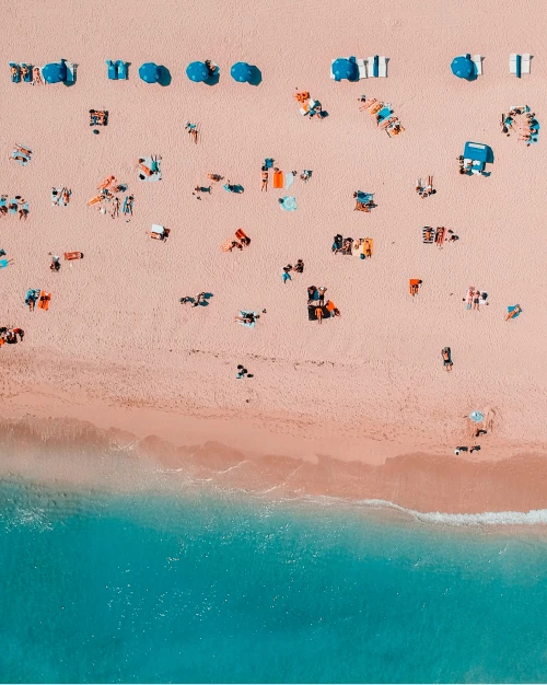 A top-down view of a busy beach with people lounging on beach towels and under umbrellas.