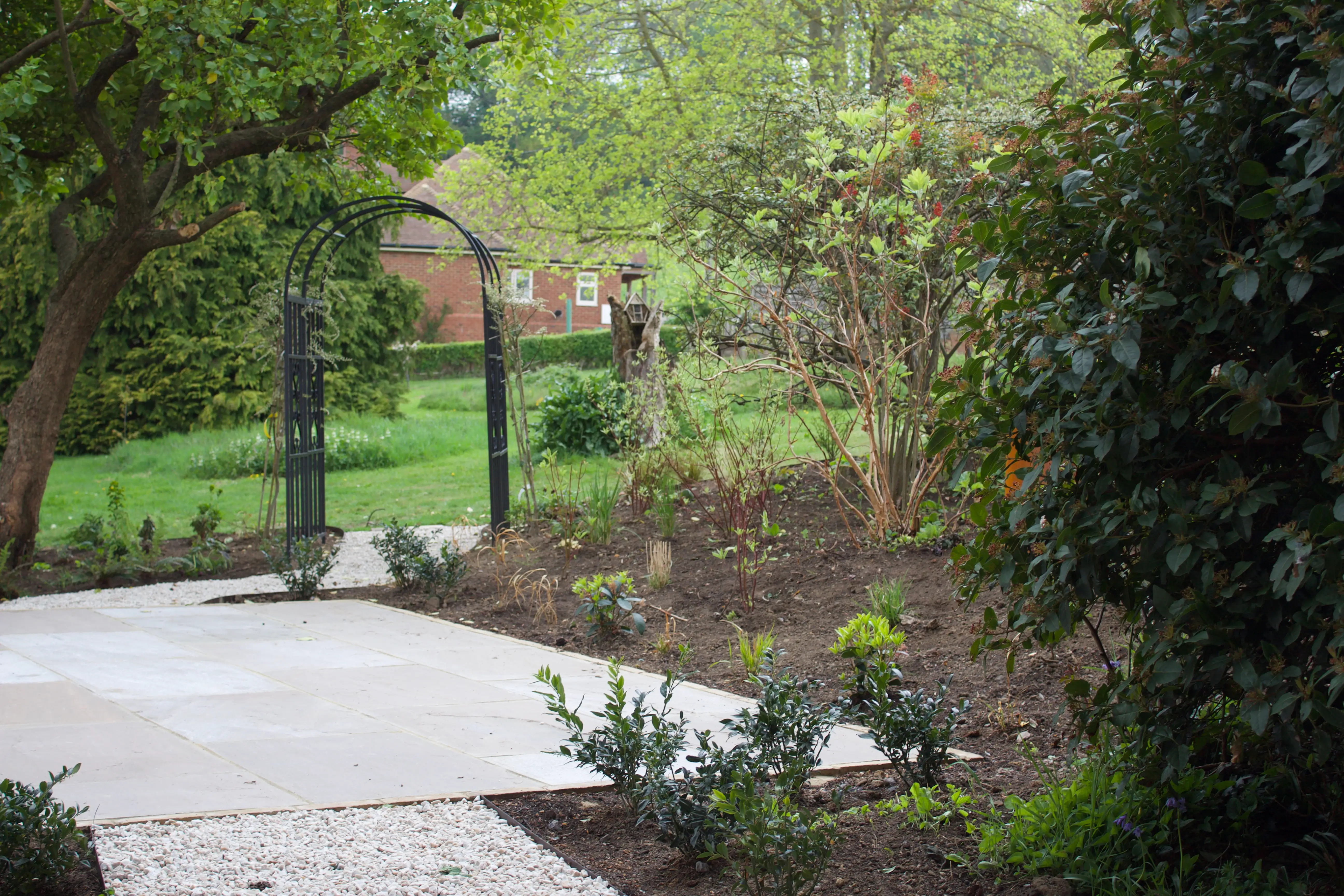 A serene garden scene featuring green grass, trees, and a pathway leading into the lush surroundings.