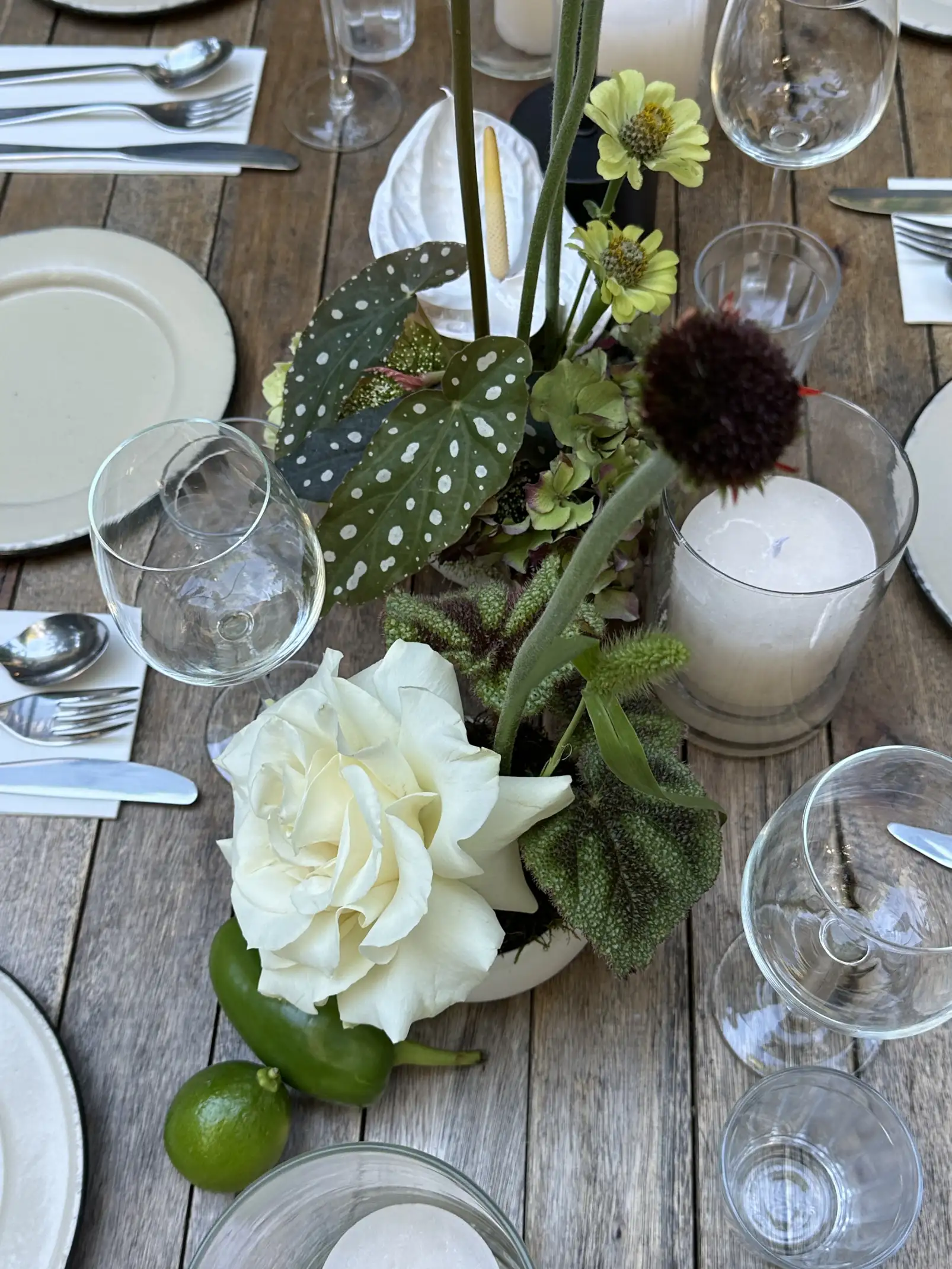 Centro de mesa con rosa blanca, follaje y limas sobre mesa rústica con vajilla neutra.