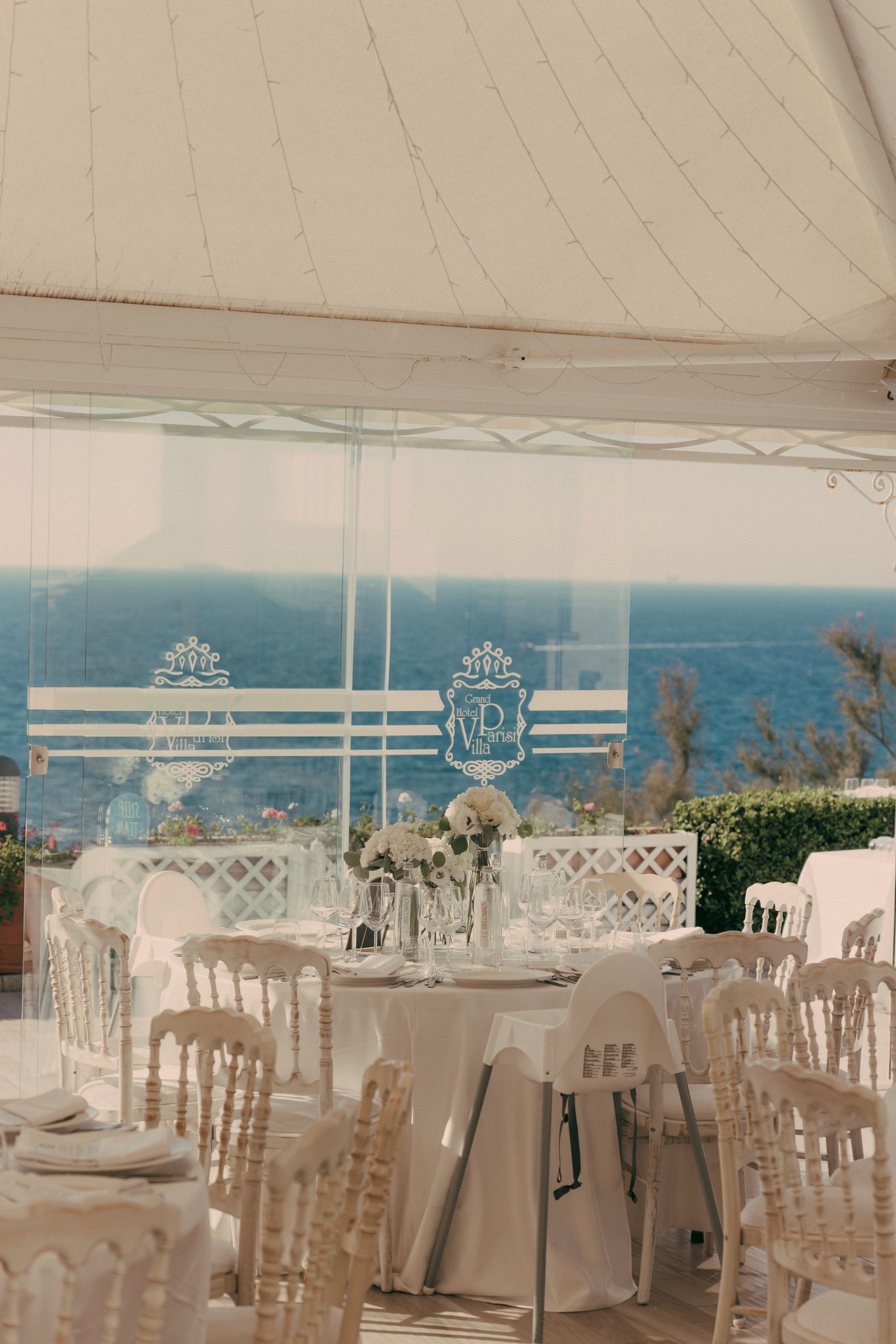 Tavoli del ricevimento sotto la tenda a Bolgheri, con vista sul mare e dettagli floreali bianchi, reportage matrimoniale