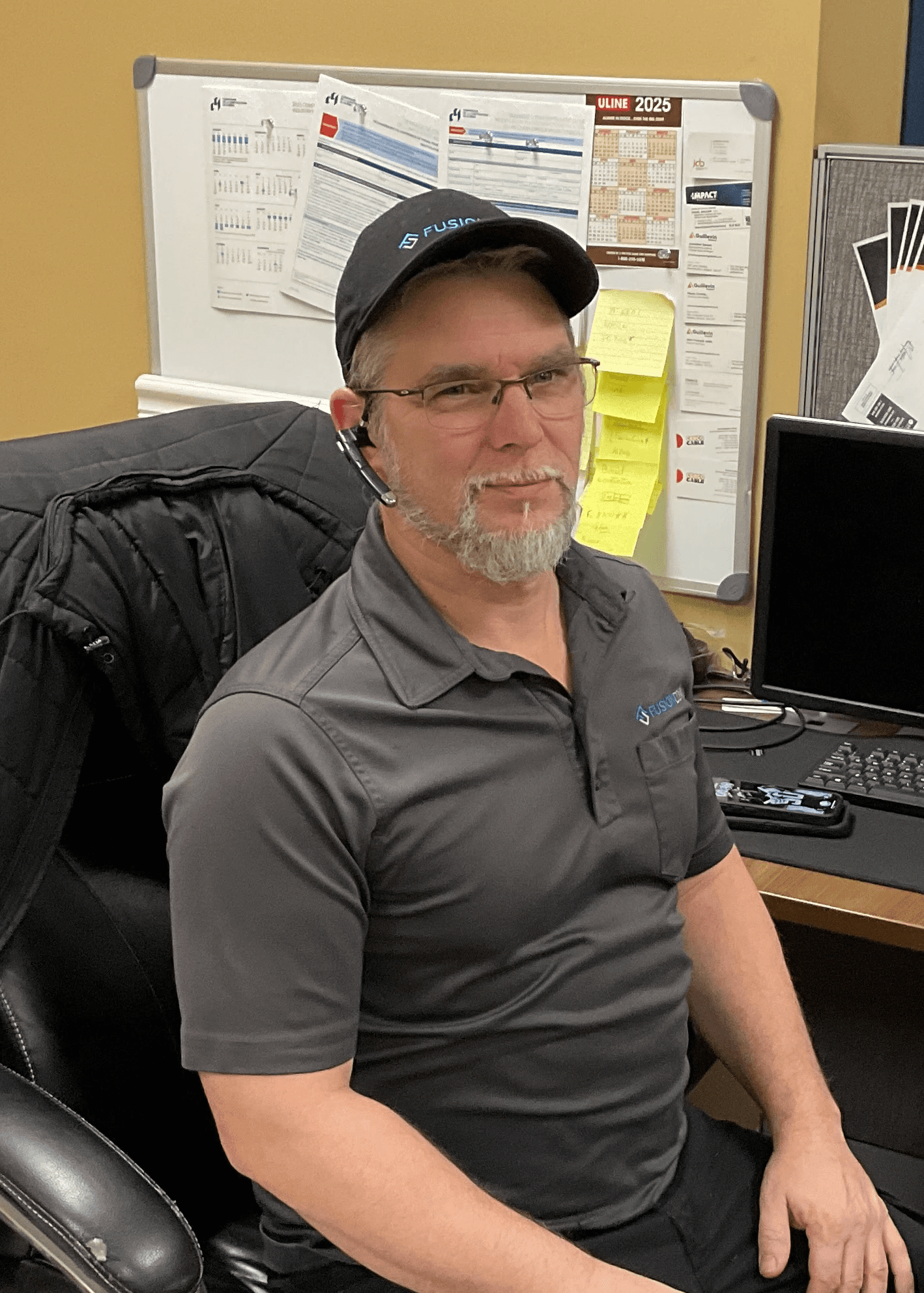 Portrait d’Eric Hamelin, employé technique, assis à son bureau avec une casquette noire.