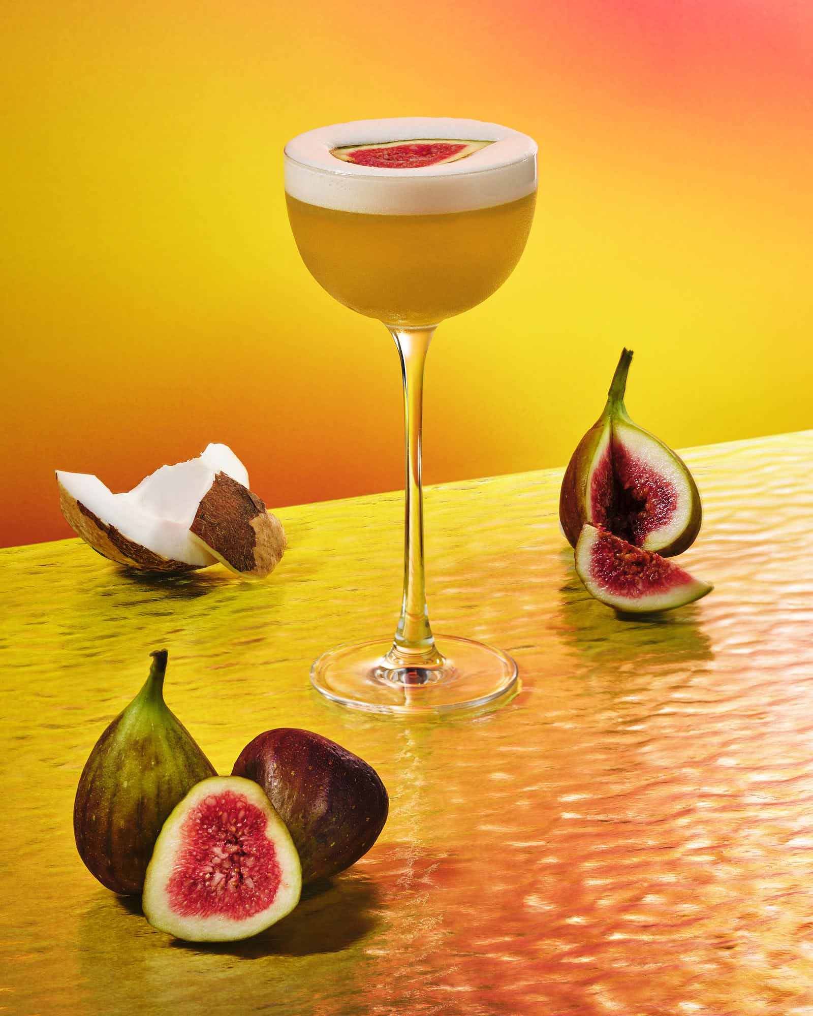 A vibrant cocktail in a glass, surrounded by fresh figs on a colorful background.