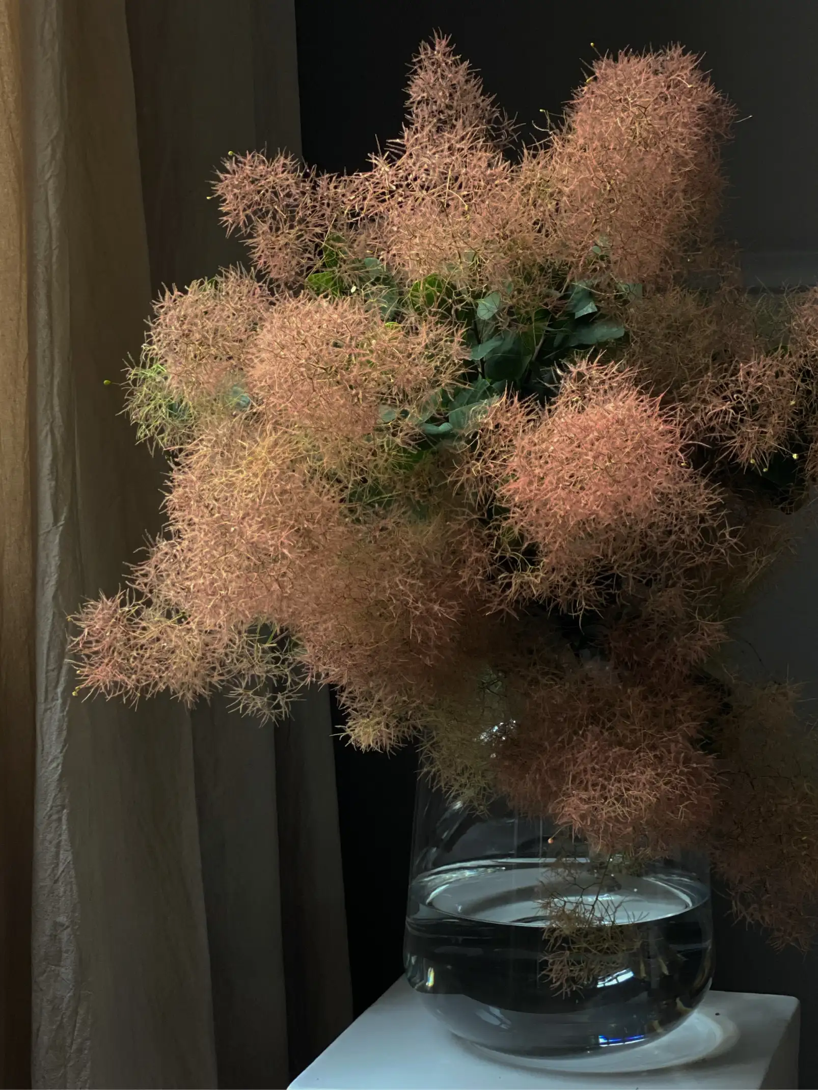 Arreglo floral de tonos ocres en jarrón de vidrio para diseñadores de interiores que buscan inspiración en composiciones naturales y texturadas.