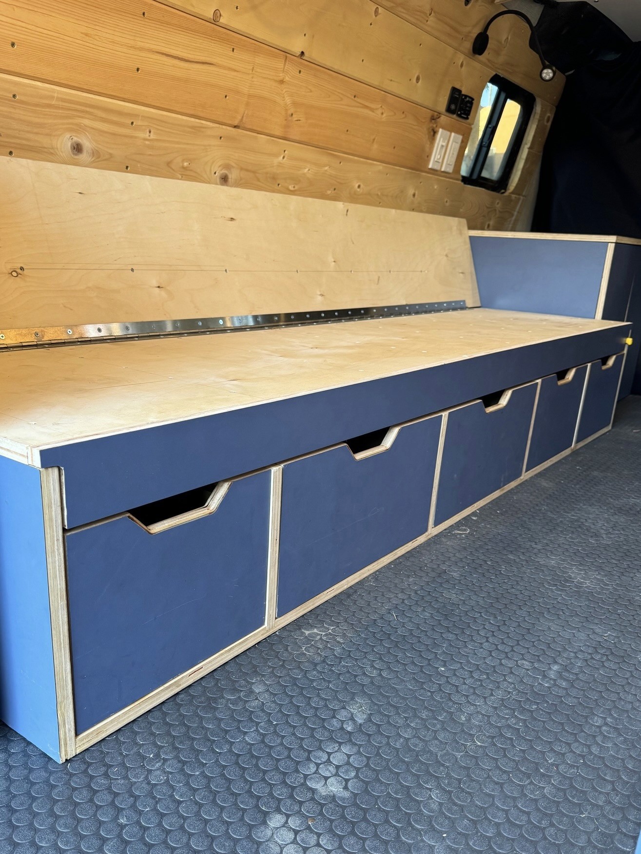 Custom van bench with blue storage drawers and a hinged wood seat