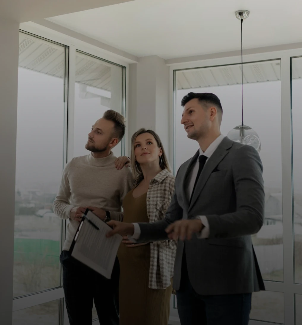 imagem de arquiteto responsável pelo projeto, trajado de terno, exibindo a casa para um casal heterossexual que está observando a casa por dentro.