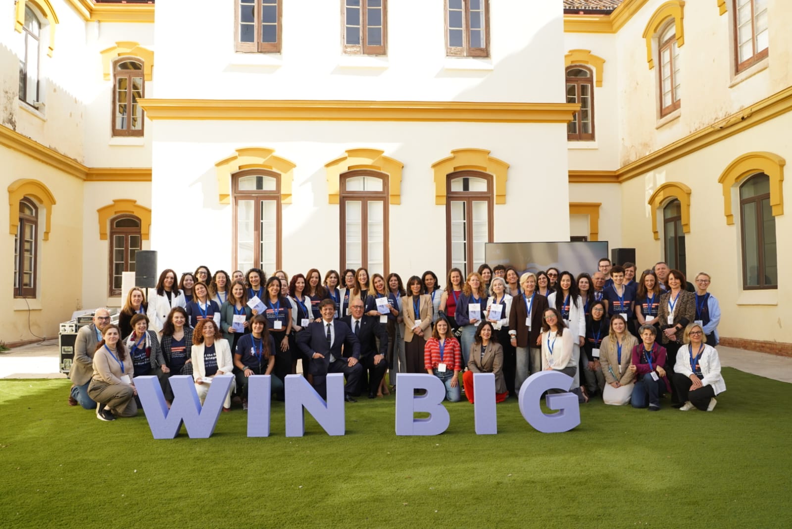 A person wearing a virtual reality headset stands in front of multiple screens, engaged in a digital experience.