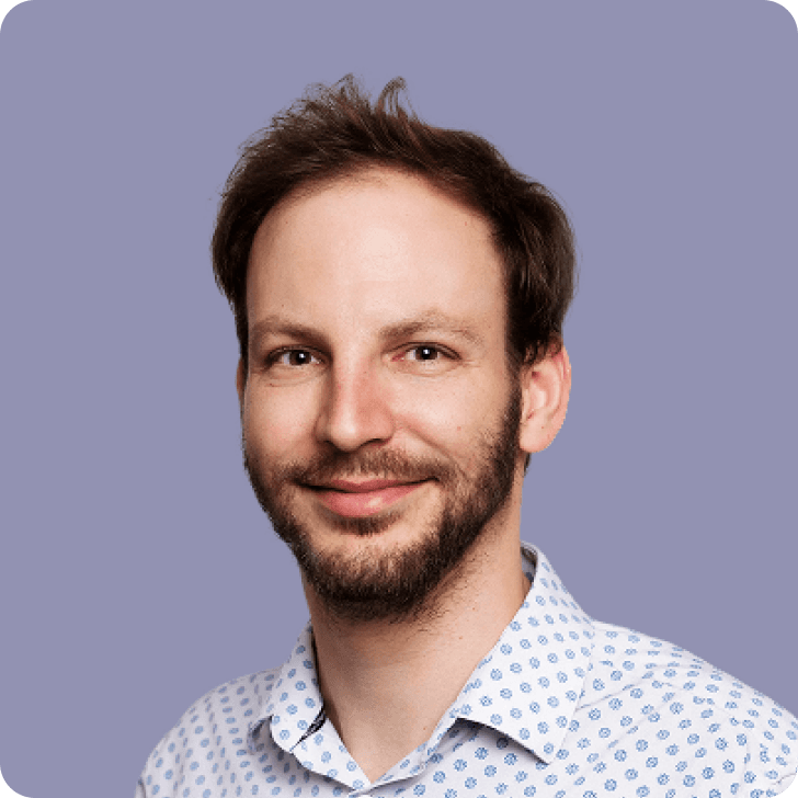 A younger man in a patterned shirt in front of a purple background