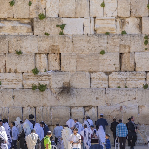 People praying at the Western Wall in Jerusalem, some wearing traditional religious garments.