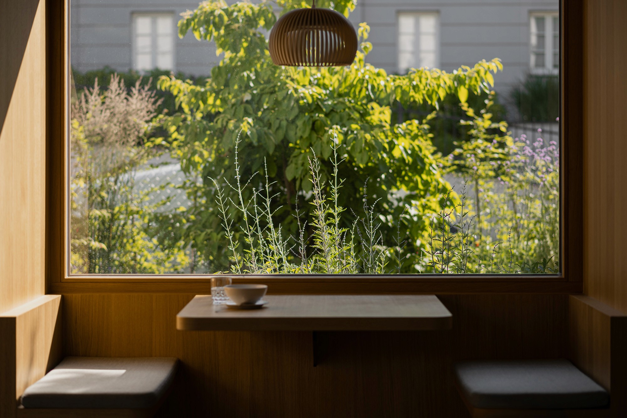 Blick aus dem Innenraum auf einen üppig bepflanzten Garten mit Sträuchern und Stauden.