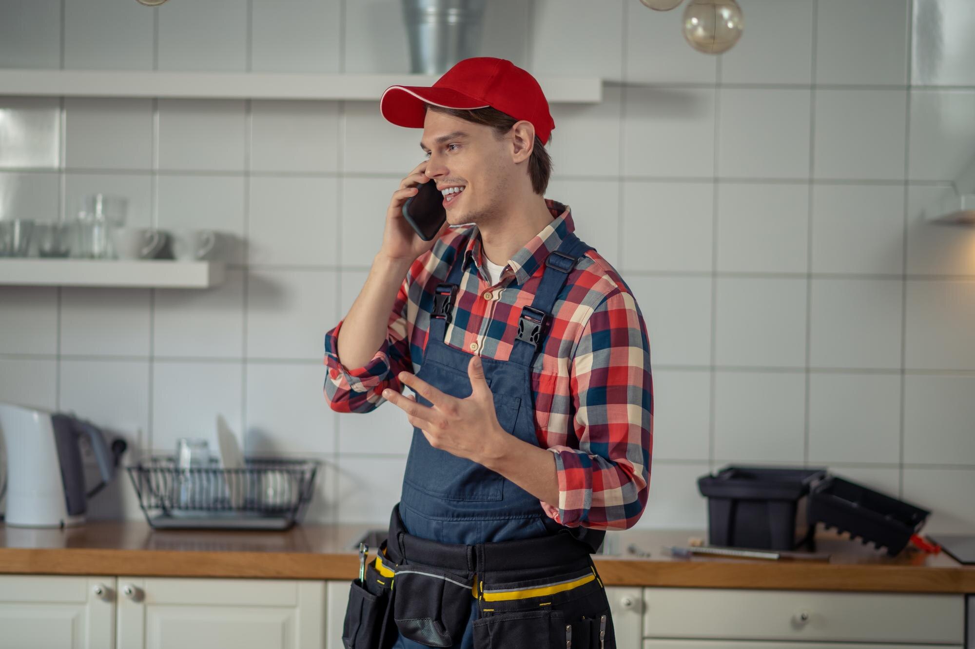 Monteur in werkoverall met gereedschapsriem telefoneert met een klant