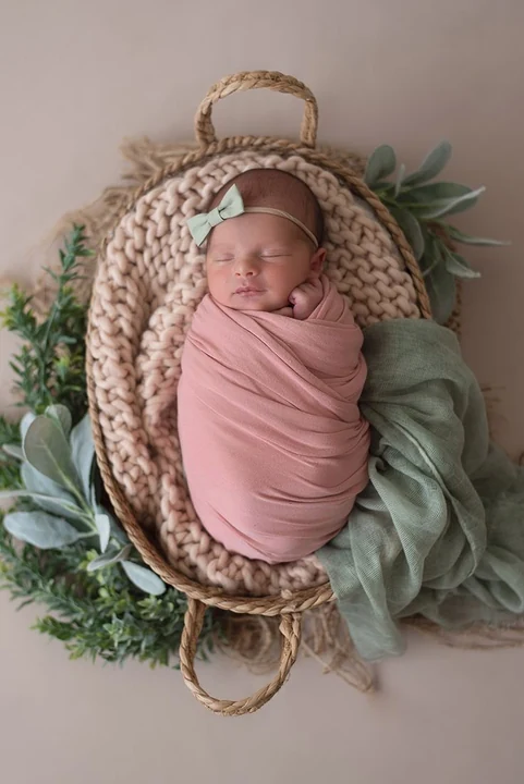 Newborn wrapped in pink cloth in a basket surrounded by greenery