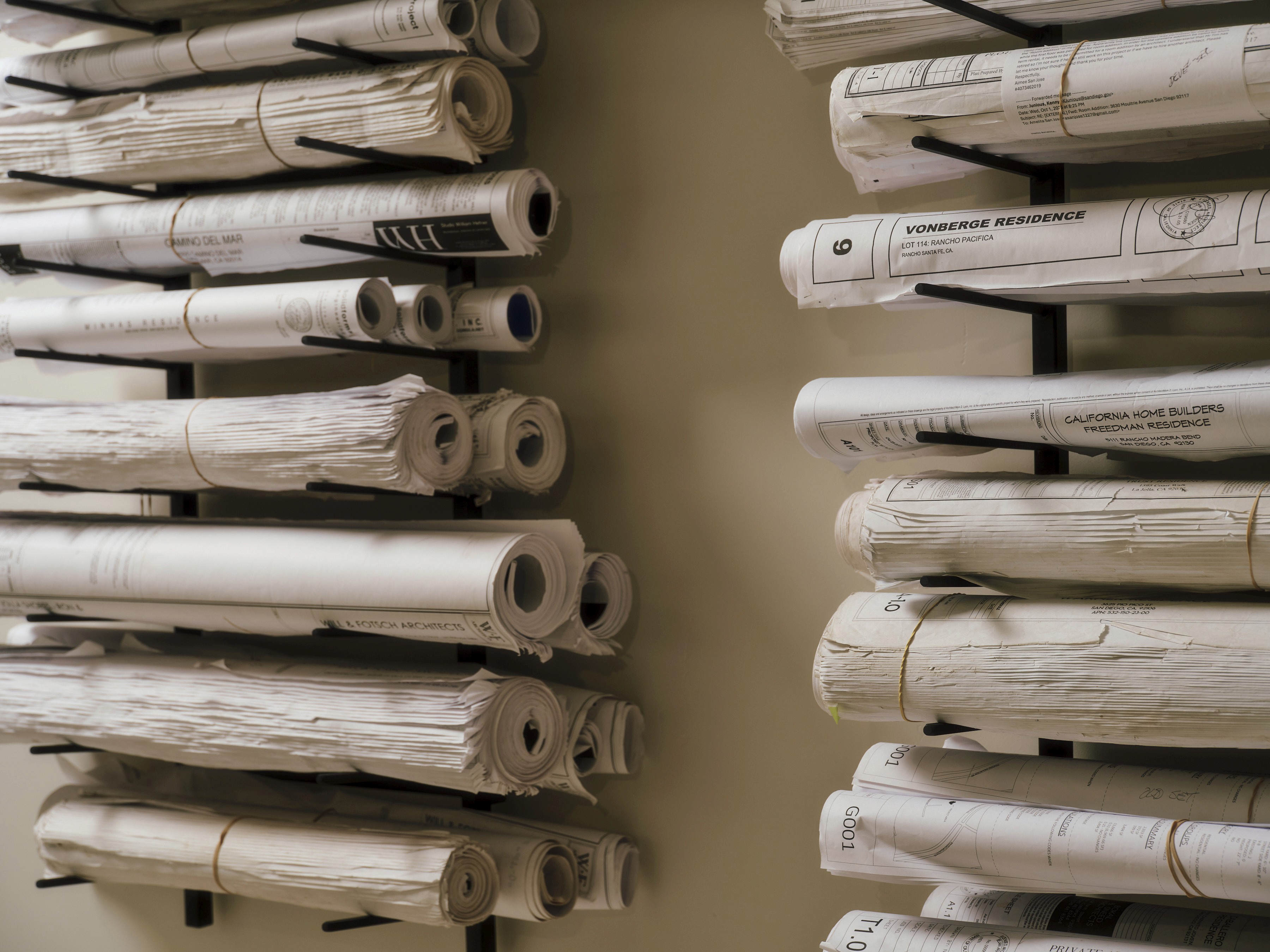 Two wall racks hold numerous rolled architectural blueprints. Visible labels include "Vonberge Residence," "California Home Builders," and "Freedman Residence."