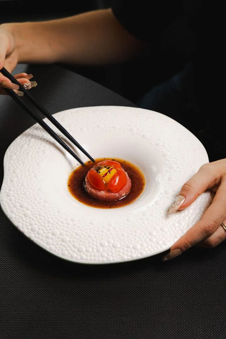 Sauce-glazed bite picked up with chopsticks from a white plate