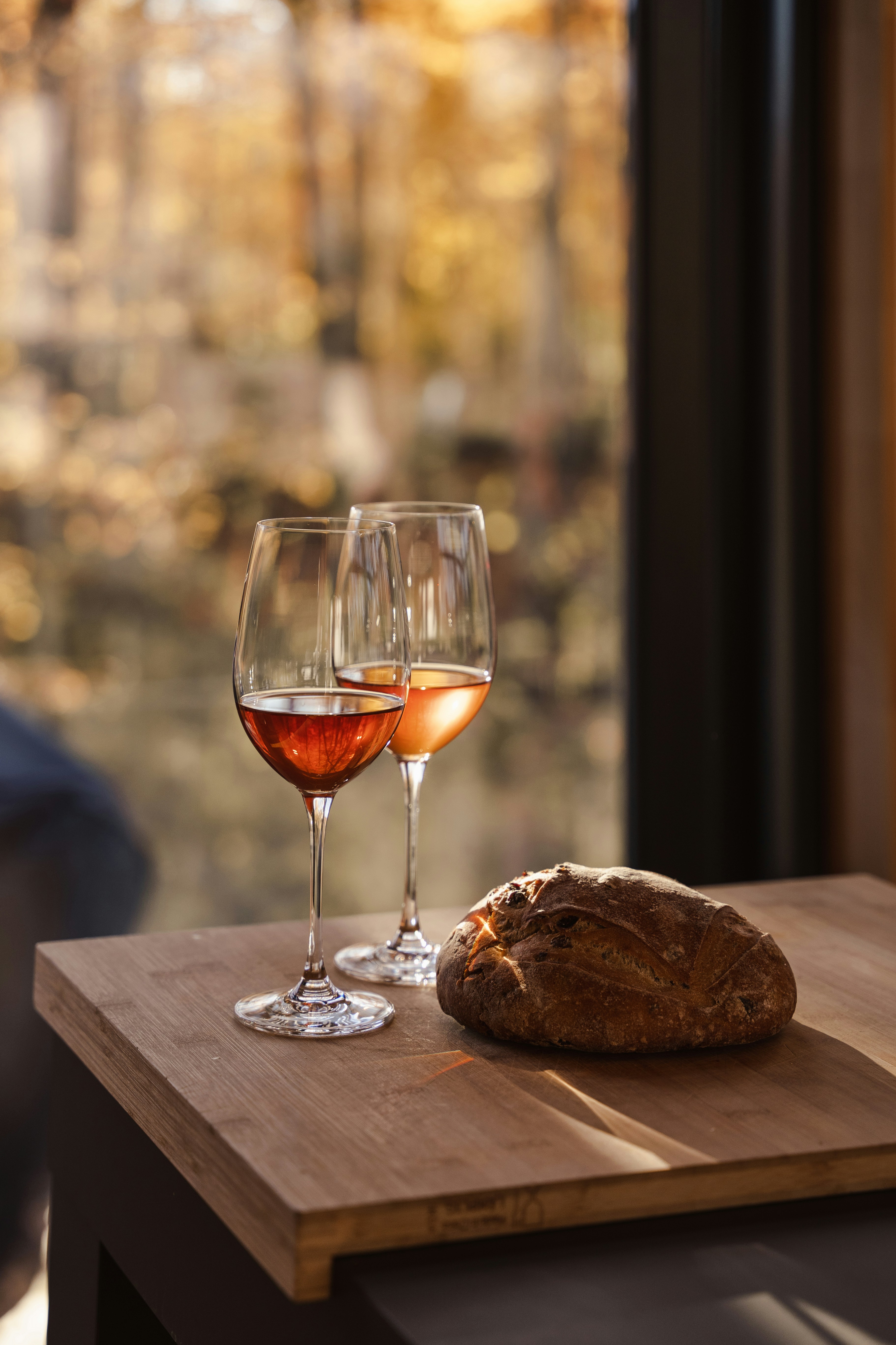 Red and orage wines in glasses by a window with view to the forest and a bread besides the wine glasses