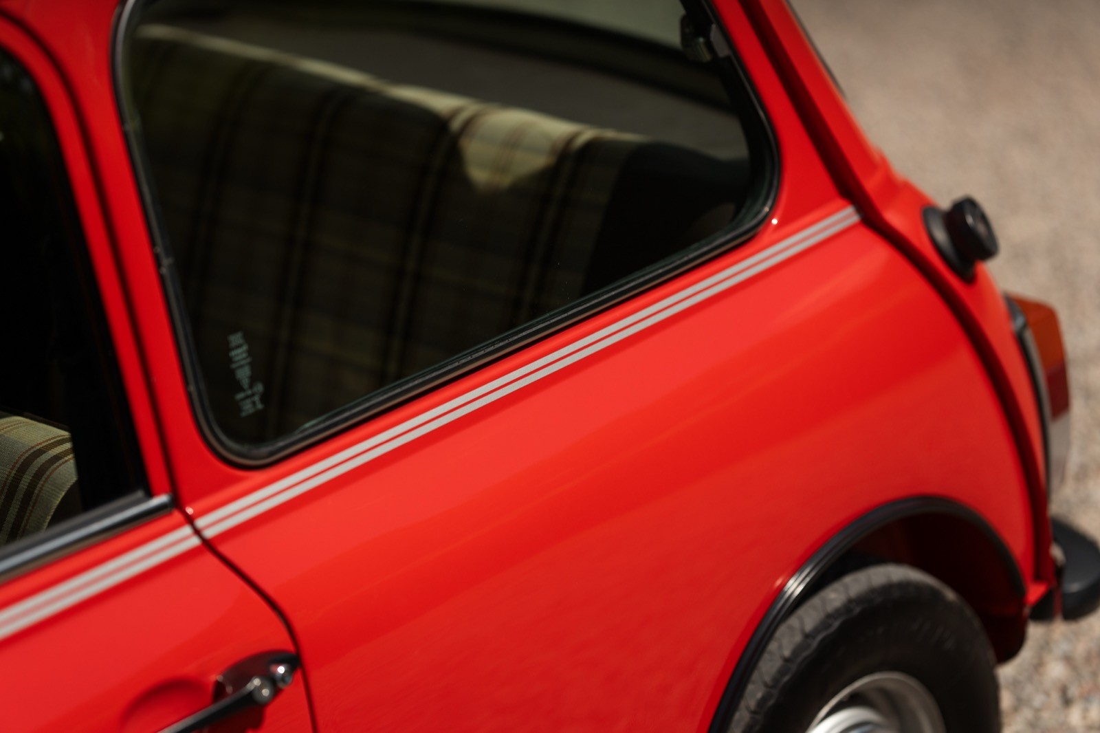 A close-up view of a red car's rear side with a partially visible window and tire.