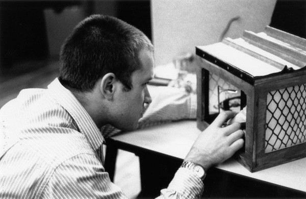 A black and white photo of a person working on a miniature city setup put in a box.