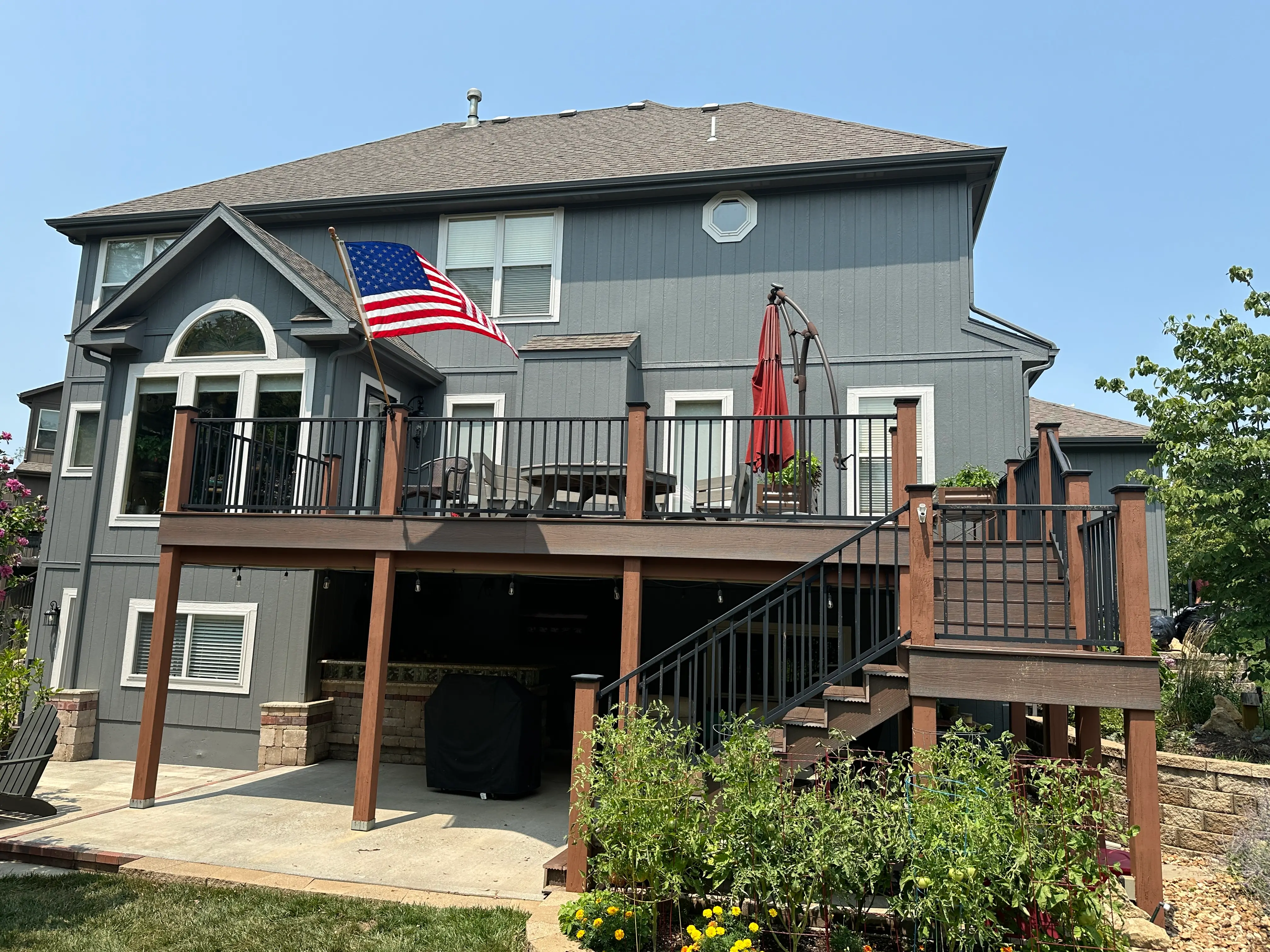 An image of a newly built deck with metal railings and an American Flag againts a grey house.