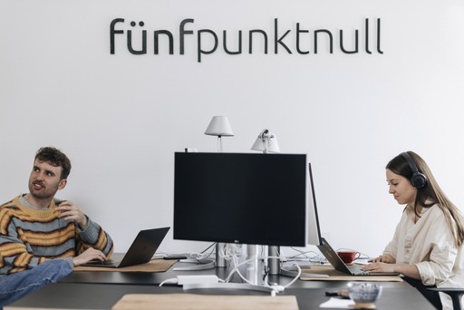 Moritz Gahm und Julia Thum von der Research- und UX-Agentur fünfpunktnull sitzen unter dem Firmenlogo an Laptops