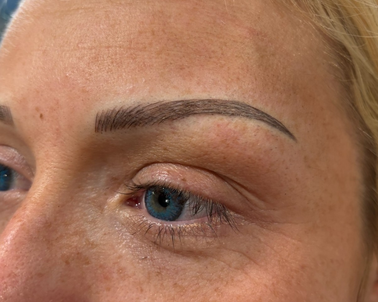 Angled view of a woman's face showing freshly microbladed eyebrows with a natural, defined shape and realistic hair strokes.