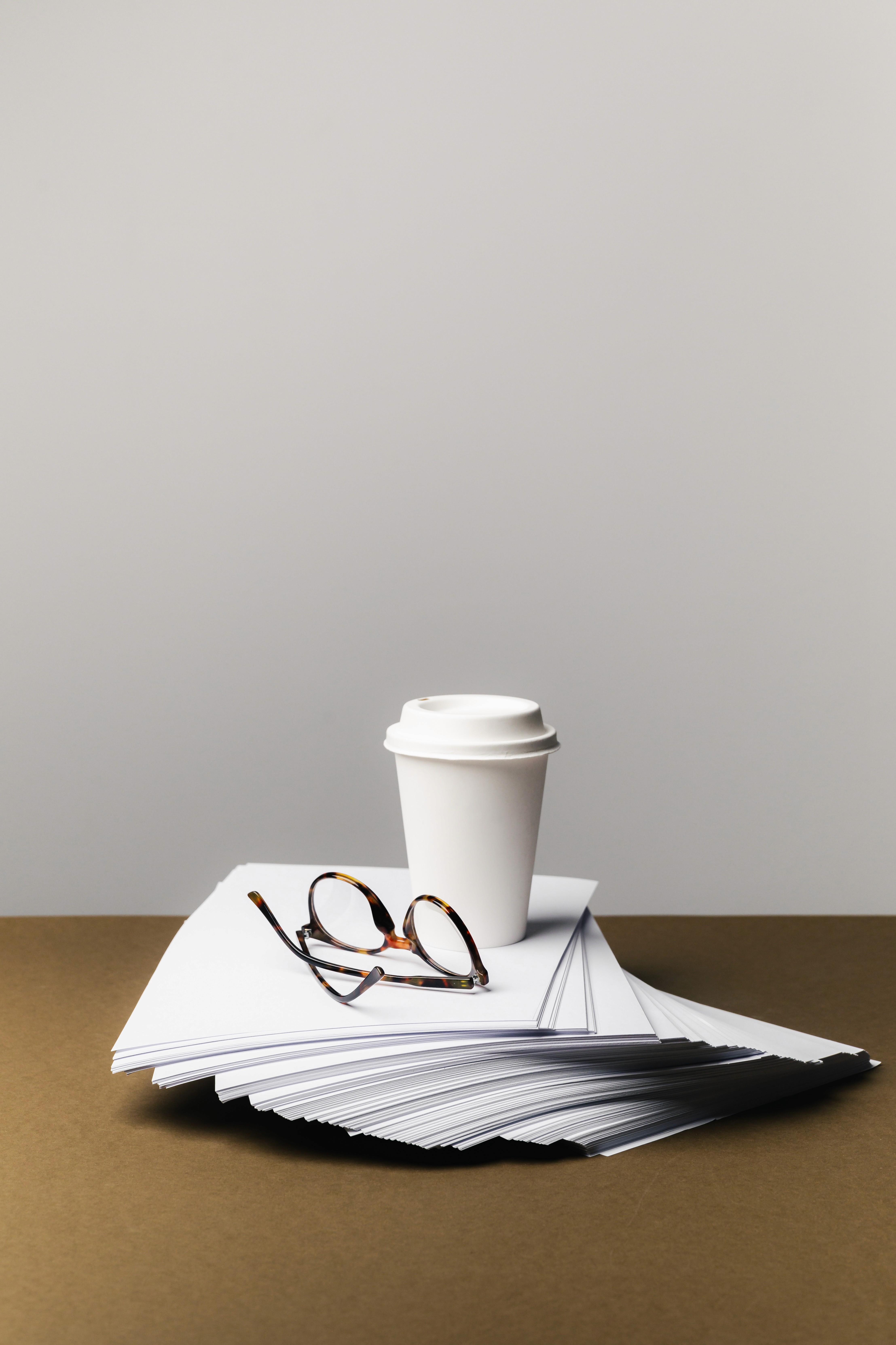 takeaway coffee cup placed on top of a stack of papers with a pair of glasses resting beside it.