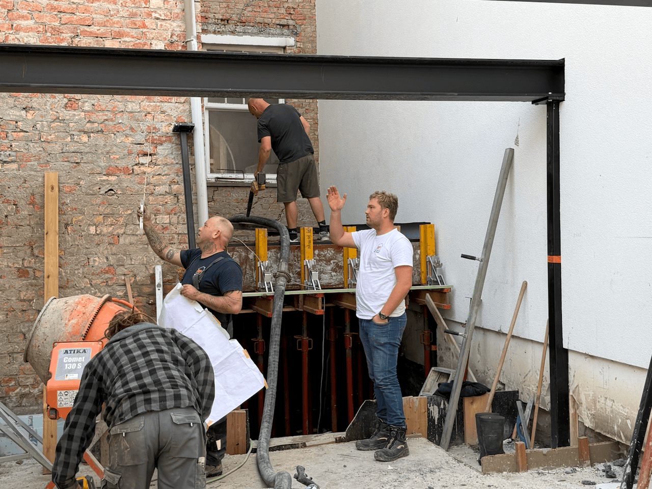 Mensen bekijken een bouwplan op een werf, met bekisting en een stalen ligger zichtbaar.