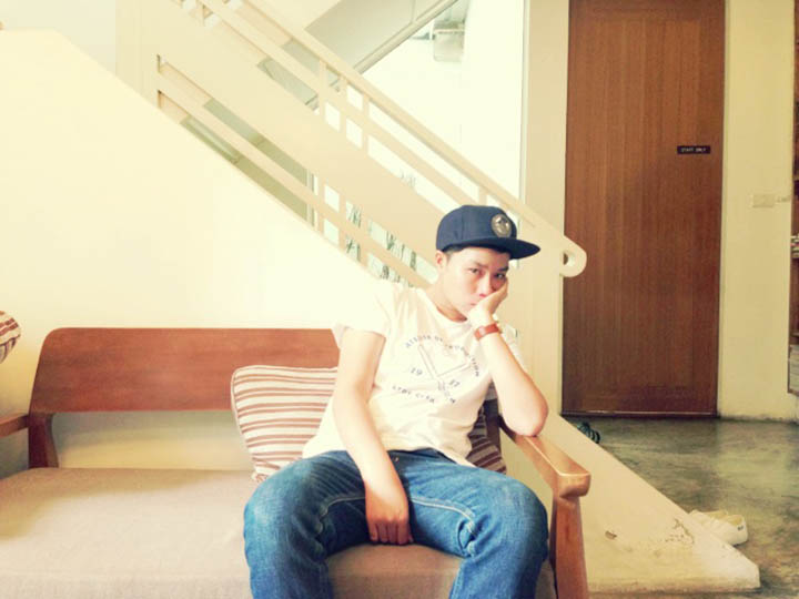 A photo of a man wearing a cape, a white t-shirt and blue jeans while sitting o a couch.