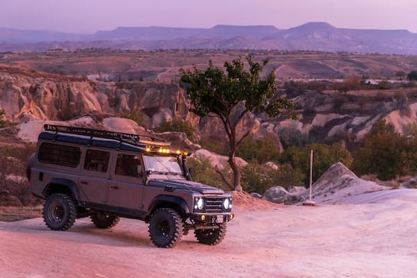 Off-road vehicle in Cappadocia, with a tree and rocky valley landscape in the background.